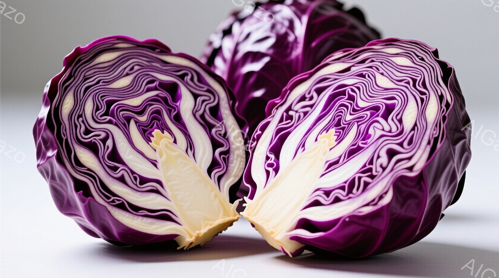 鮮やかな紫色のキャベツが半分にカットされたものが、写真中央に大きく配置されている。キャベツの断面からは、クリーム色の葉脈が放射状に広がり、美しいコントラストを生み出している。背景は白く、キャベツの鮮やかな色が際立っており、全体的にシンプルで清潔感のある印象を与える。