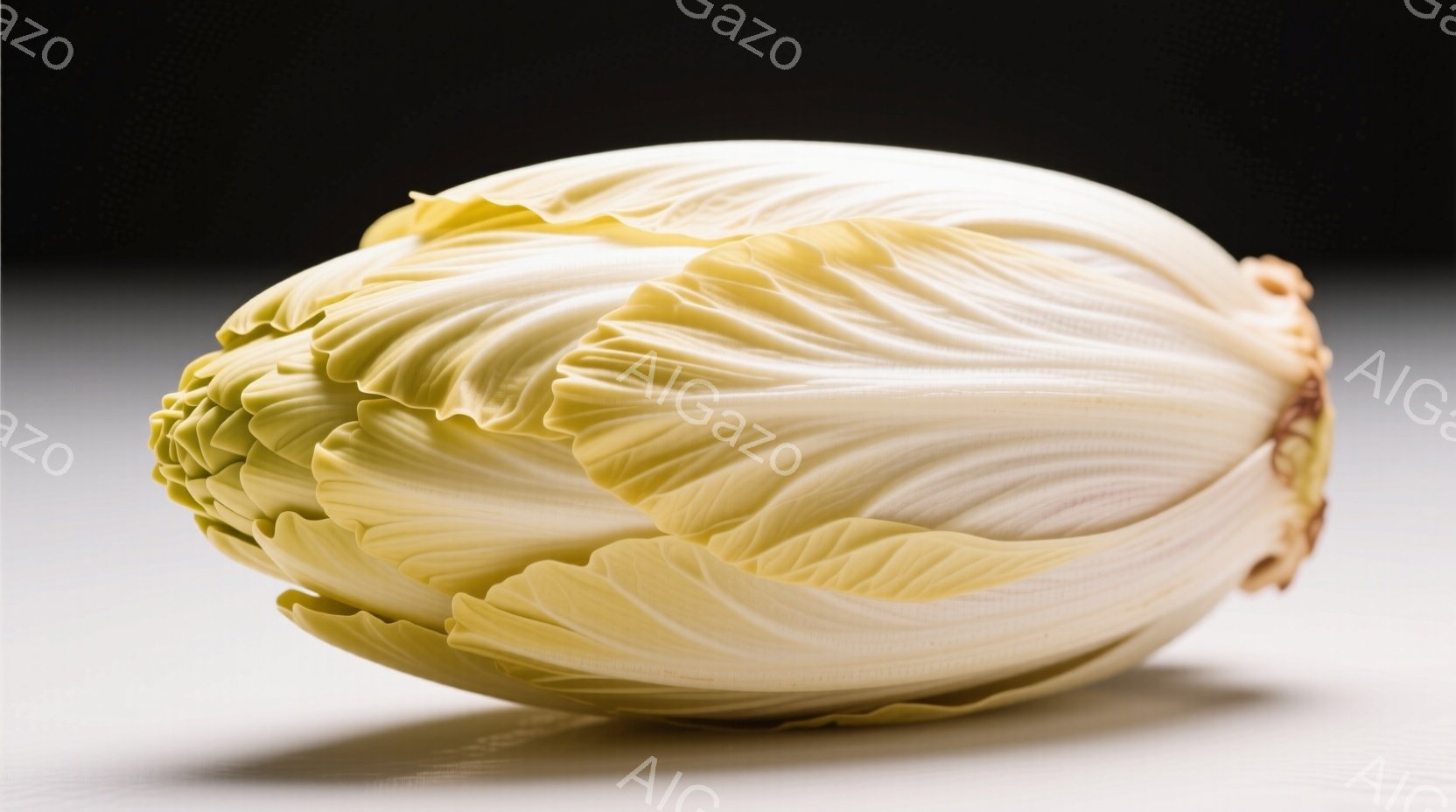白くて緑がかったキャベツが、白い表面の上に置かれています。葉は互いに重なり合い、花のような形を作り出しています。背景は暗く、キャベツが際立っています。