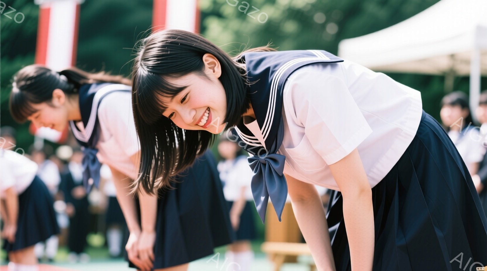 制服姿の女子学生たちが、体育館のような場所で一斉に前屈をしている様子が写っている。紺色のスカートと白いセーラーシャツを着ており、笑顔の生徒もいる。背景には緑の芝生と建物が見え、晴天で明るい雰囲気である。