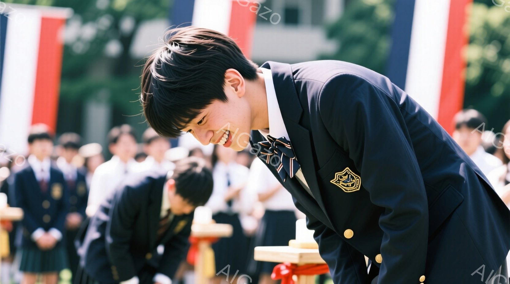 制服を着た男子学生が深くお辞儀をしている様子が捉えられています。彼は黒いブレザー、白いシャツ、ネクタイを着用し、髪は短く整えられています。背景には他の学生たちが制服姿で立ち、緑豊かな自然と建物が見え、晴れた日の式典のような雰囲気が漂っています。