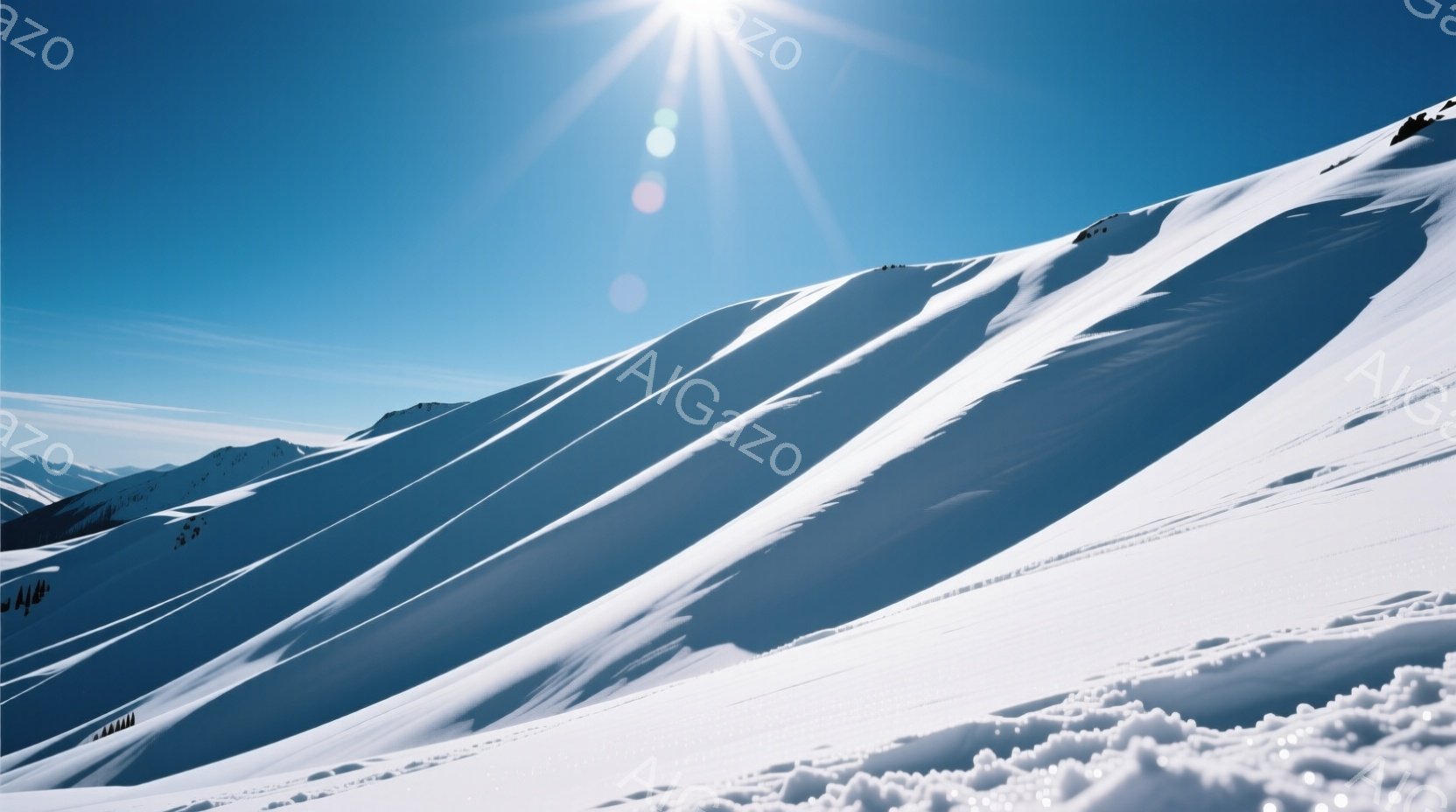 白い雪に覆われた山々が、強い日差しのもと、壮大な景色を広げている。雪面には滑走路のような線が刻まれ、スキーヤーやスノーボーダーが利用した痕跡が見られる。空は澄み切った青色で、冬の静寂と雄大さを感じさせる、爽やかな光景である。