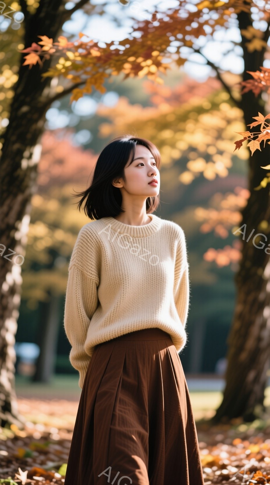 明るいクリーム色のニットセーターと、深みのある茶色のフレアスカートを身につけた若い女性が写っている。彼女は少し上を見つめ、穏やかで物憂げな表情を浮かべている。背景には紅葉した木々と緑の芝生が広がり、秋の穏やかな陽光が彼女を照らし出している。