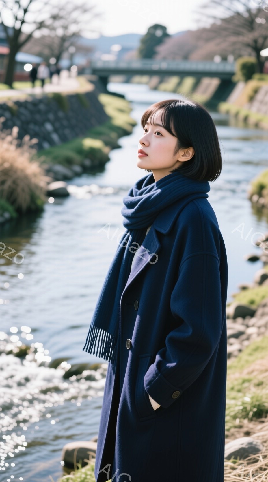 深い藍色のコートとスカーフを身につけた女性が、川沿いを歩いている様子が写っている。彼女は黒髪のショートボブで、少し憂いを帯びた表情で遠くを見つめている。背景には、石積みの川岸と穏やかな川の流れ、そして - AI生成フリー素材