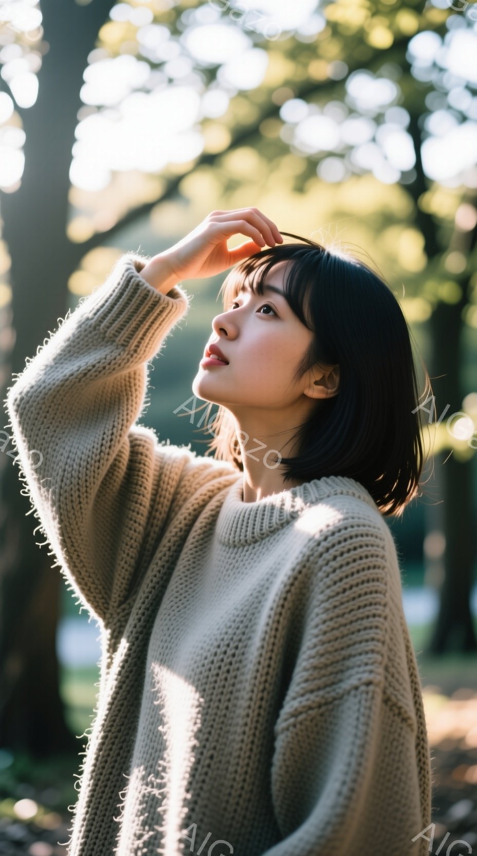 短い黒髪の女性が、ベージュ色のざっくりとしたニットを着て、片手を頭に当てて少し上を見ている。背景には緑豊かな木々が見え、太陽の光が木々の間から差し込み、柔らかい雰囲気を醸し出している。全体的に、自然の中でリラックスした穏やかな瞬間を捉えた写真である。