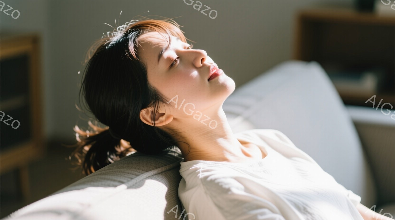 明るい光の中で、女性がソファに横たわり、目を閉じてリラックスしている様子が写っている。短いダークブラウンのヘアスタイルで、白いトップスを着ており、穏やかな表情をしている。背景にはぼやけた家具が見え、全 - AI生成フリー素材