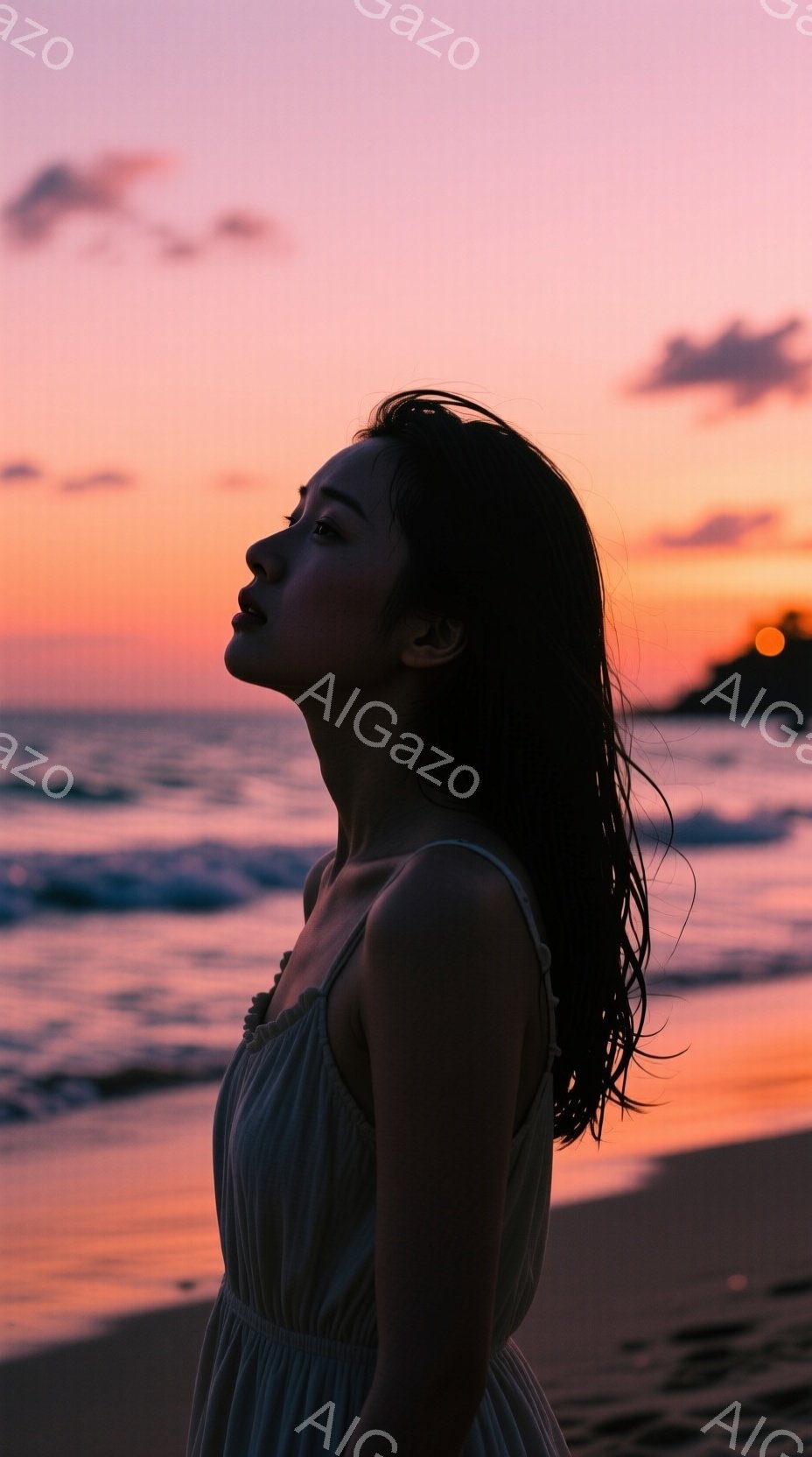 長い黒髪を風になびかせながら、女性が夕暮れのビーチで横顔を見せている。淡い色のストラップレスのドレスを着ており、穏やかで少し物憂げな表情をしている。背景には、オレンジとピンクの色合いが美しい夕焼け空と、穏やかな波が広がる海が広がっている。
