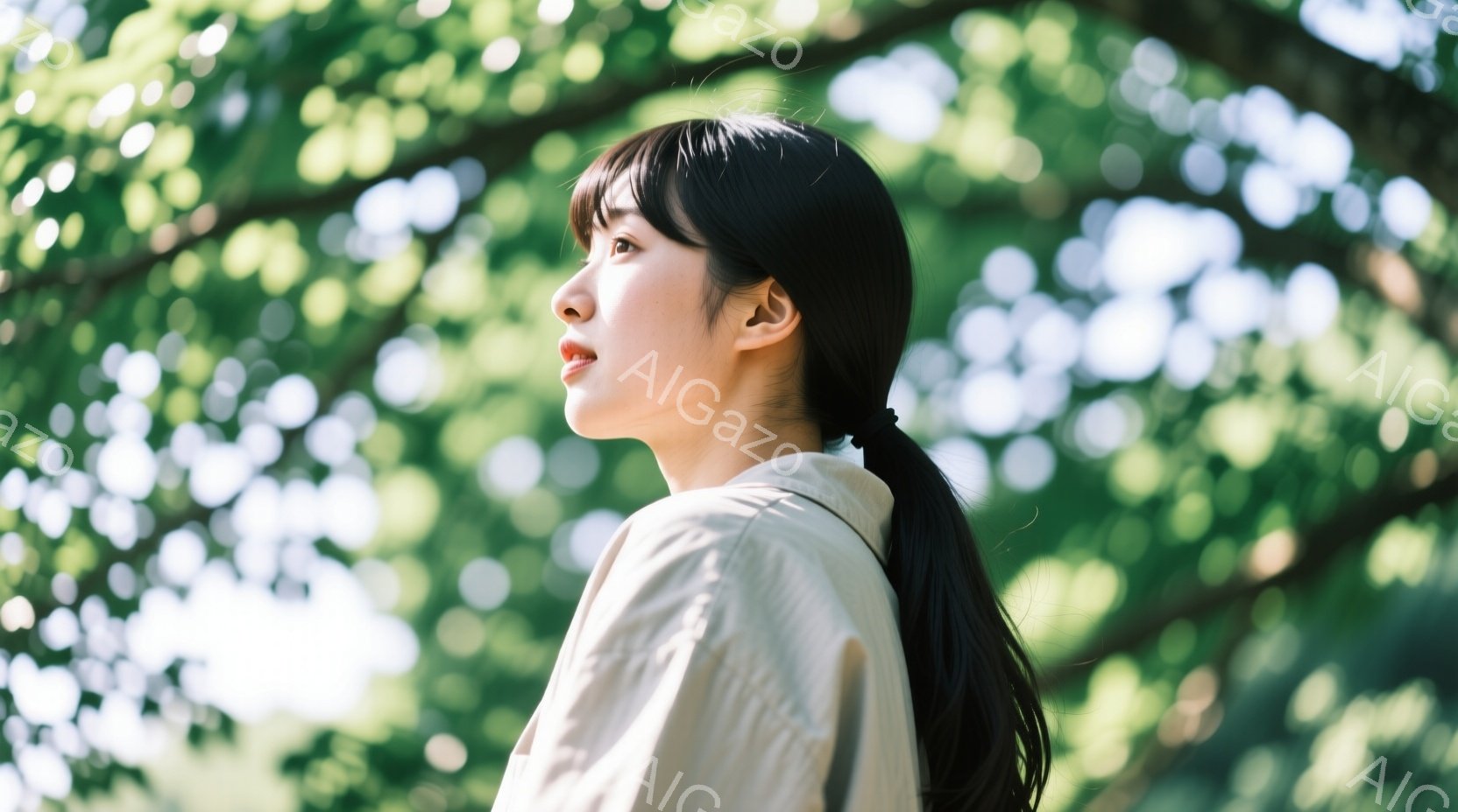 黒髪をポニーテールにした若い女性が、やや横を向いて遠くを見つめている。ベージュ色のシャツを着ており、表情は穏やかで、どこか物憂げな雰囲気を漂わせている。背景には緑豊かな木々が広がり、太陽の光が葉の間から差し込み、柔らかく優しい印象を与えている。