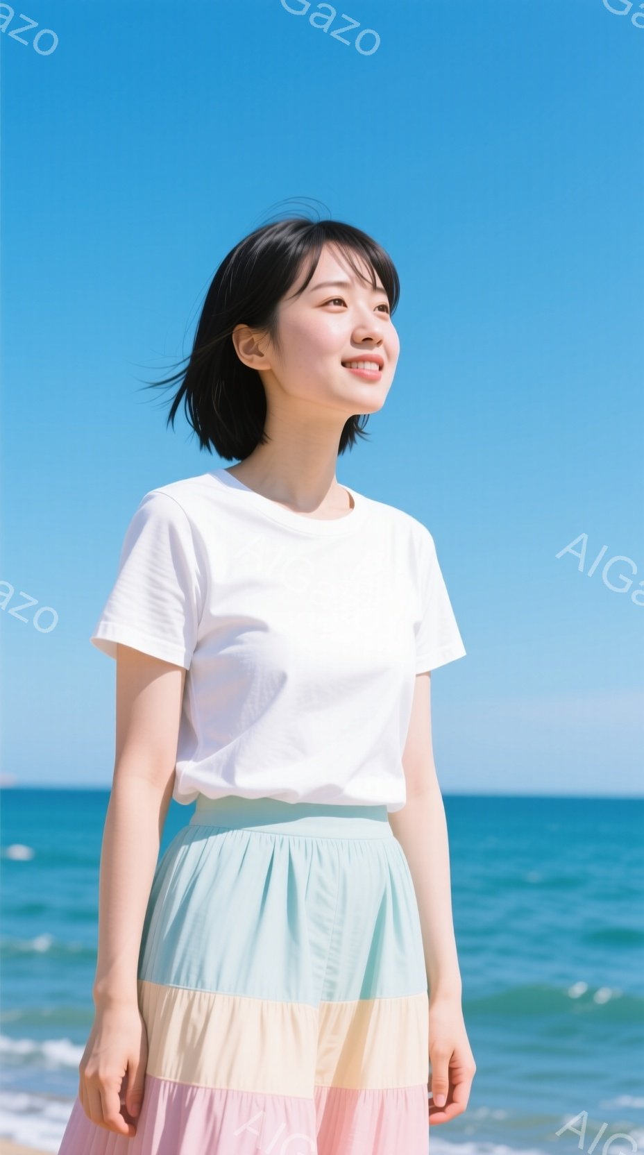 明るい青空とエメラルドグリーンの海を背景に、女性が写っている。白いTシャツに、パステルカラーのブロック柄のロングスカートを着用し、髪は短く黒髪で、少し微笑んでいる。彼女はわずかに顔を上げ、リラックスした姿勢で遠くを見つめている様子で、穏やかで爽やかな雰囲気が漂っている。