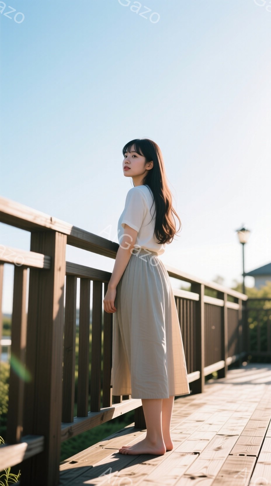 明るい日差しの下、女性が木製の橋の上に立っている。彼女はオフホワイトのTシャツとベージュのミモレ丈スカートを身に着け、足は裸足である。背景には緑豊かな自然と建物の屋根が見え、穏やかでリラックスした雰囲気が漂っている。