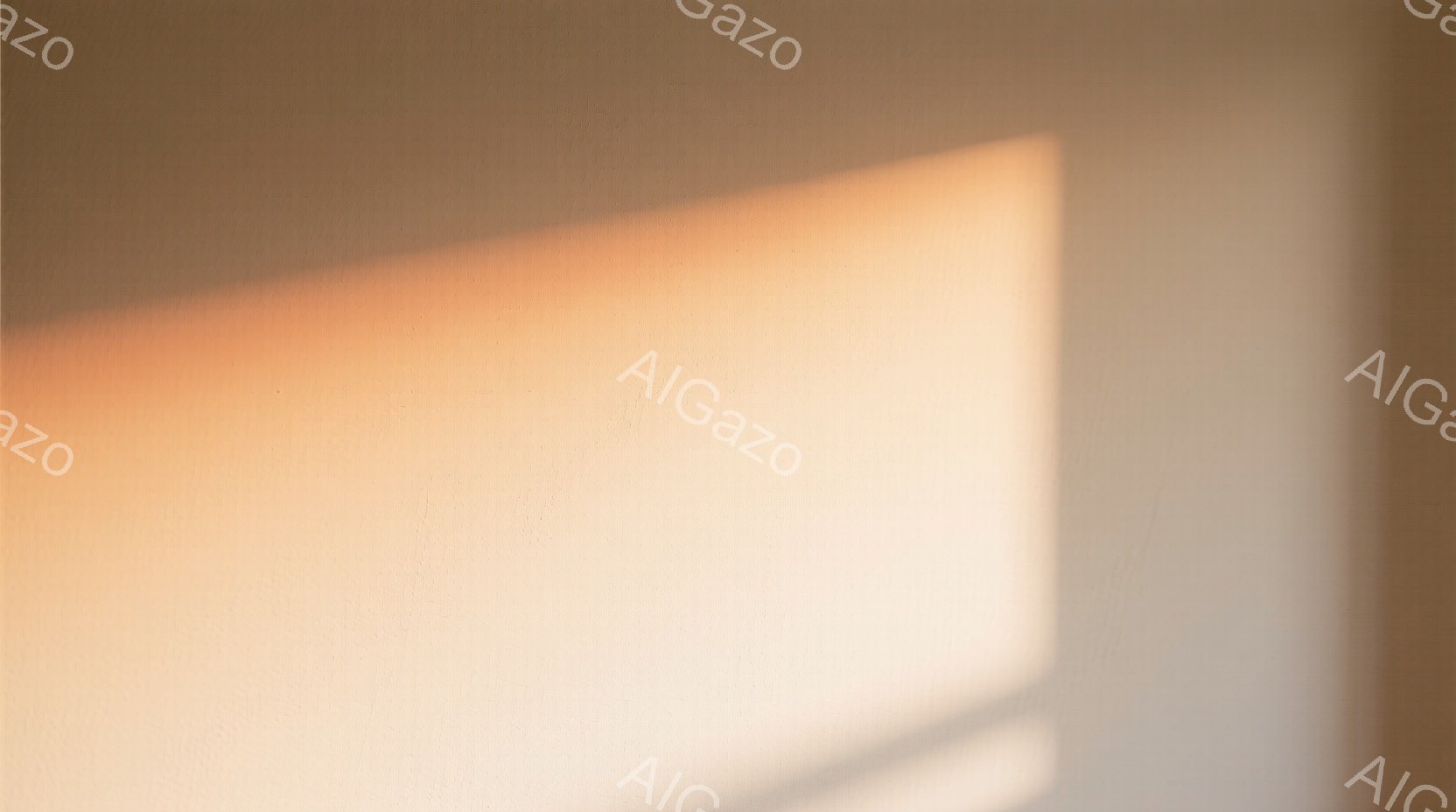 画像は、壁に映る柔らかなオレンジ色の光のグラデーションが印象的です。壁はクリーム色で、わずかなテクスチャが見られます。全体的に暖かく穏やかな雰囲気が漂い、静けさを感じさせます。