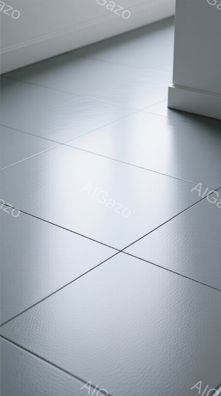 画像は灰色のタイル張りの床の一部を捉えており、タイルの目地がはっきりと確認できます。床はわずかに光沢があり、薄い光が反射して、モダンでシンプルな印象を与えます。画面の右下には白い壁の一部が写り込んでおり、背景は無機質で落ち着いた雰囲気を醸し出しています。