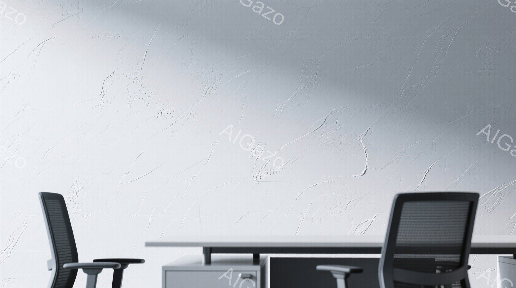 画像には、オフィスの一角が写っており、白を基調とした壁が特徴的です。手前には黒いオフィスチェアが二脚、そして白いデスクとキャビネットが配置されています。壁には独特のテクスチャがあり、現代的でミニマルな雰囲気を醸し出しています。