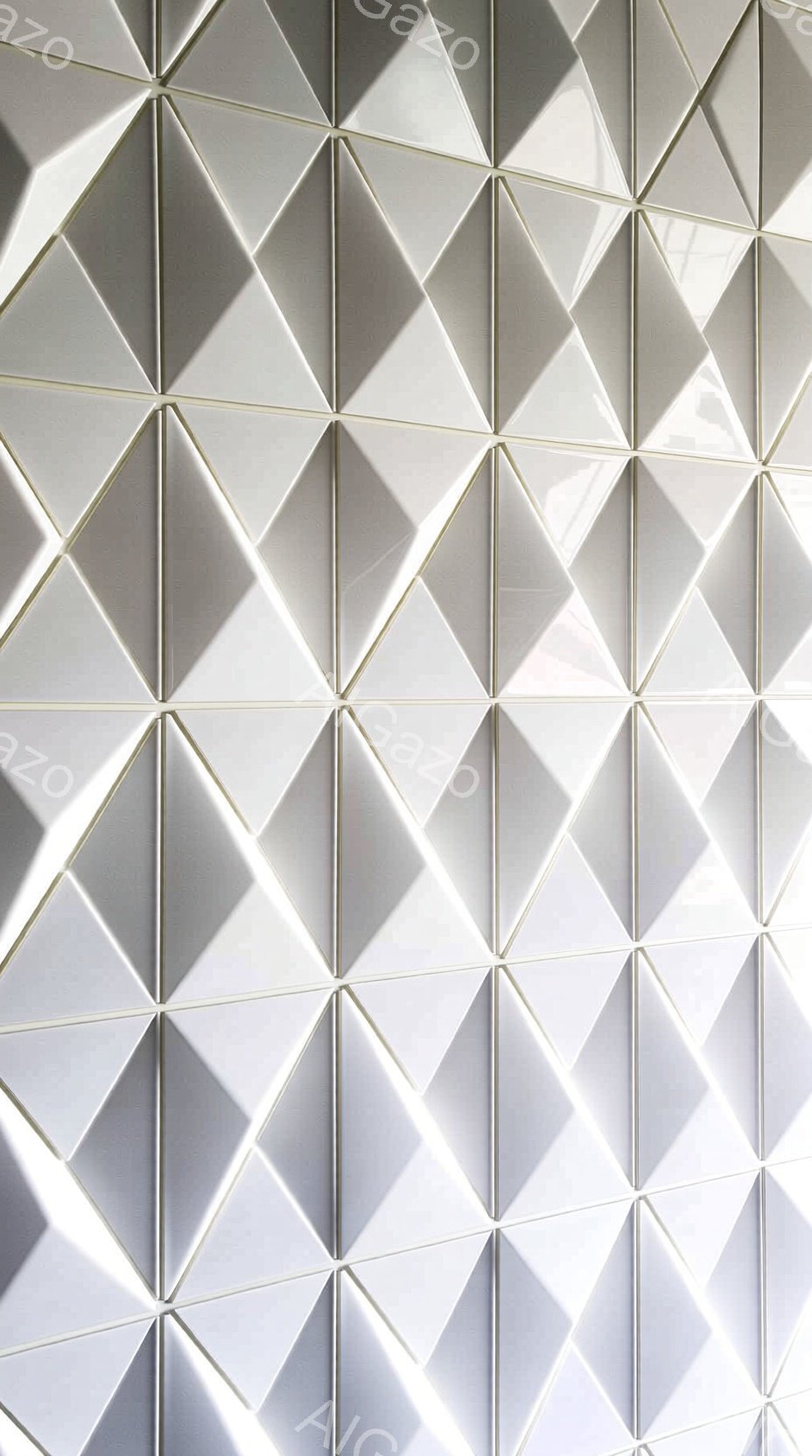 この画像は、三角形のタイルが規則的に並んだ壁面のクローズアップです。各タイルは光沢があり、立体的な陰影が特徴的で、光が当たると微妙なグラデーションを生み出しています。全体的に冷たくモダンな雰囲気で、幾 - AI生成フリー素材