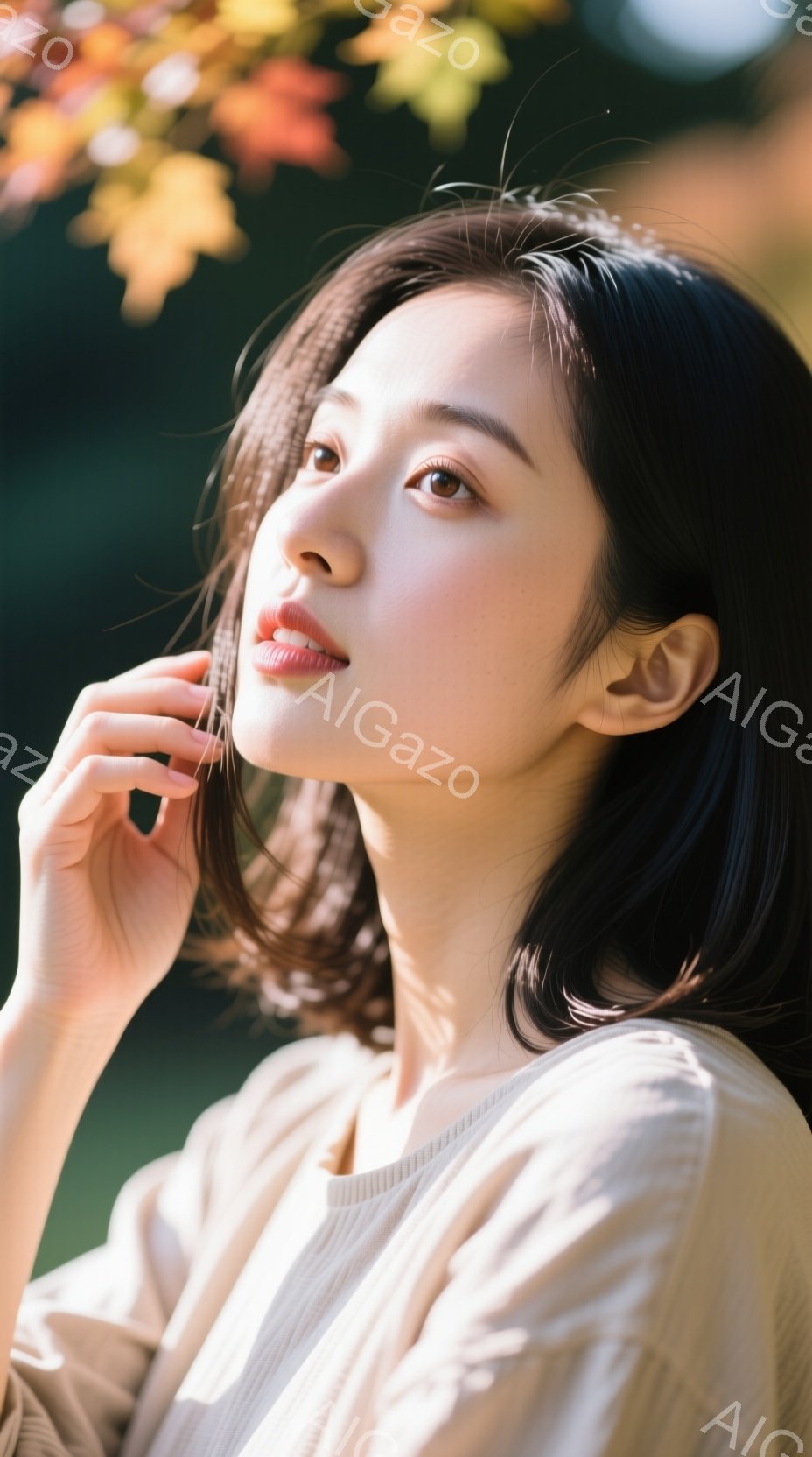 画像は、ベージュ系のニットを着た若い女性を捉えています。彼女は少し上を見上げ、指を頬に当てて物思いにふけっているような表情をしています。背景には緑とオレンジ色の葉がぼやけており、秋の穏やかな雰囲気を醸 - AI生成フリー素材