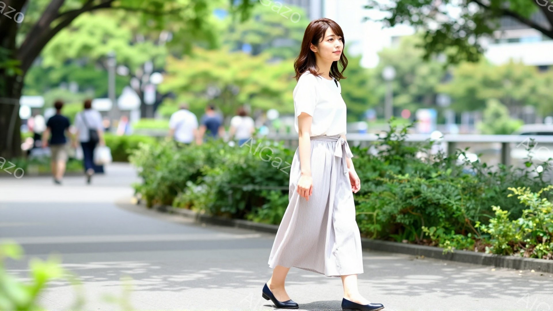 この女性は、ストライプのワイドパンツと白いブラウスを着て、歩いています。彼女は黒髪のロングヘアで、少し微笑んでいるようです。背景には緑豊かな木々と歩道、そして遠くに見える建物があり、晴れた日の穏やかな雰囲気を醸し出しています。