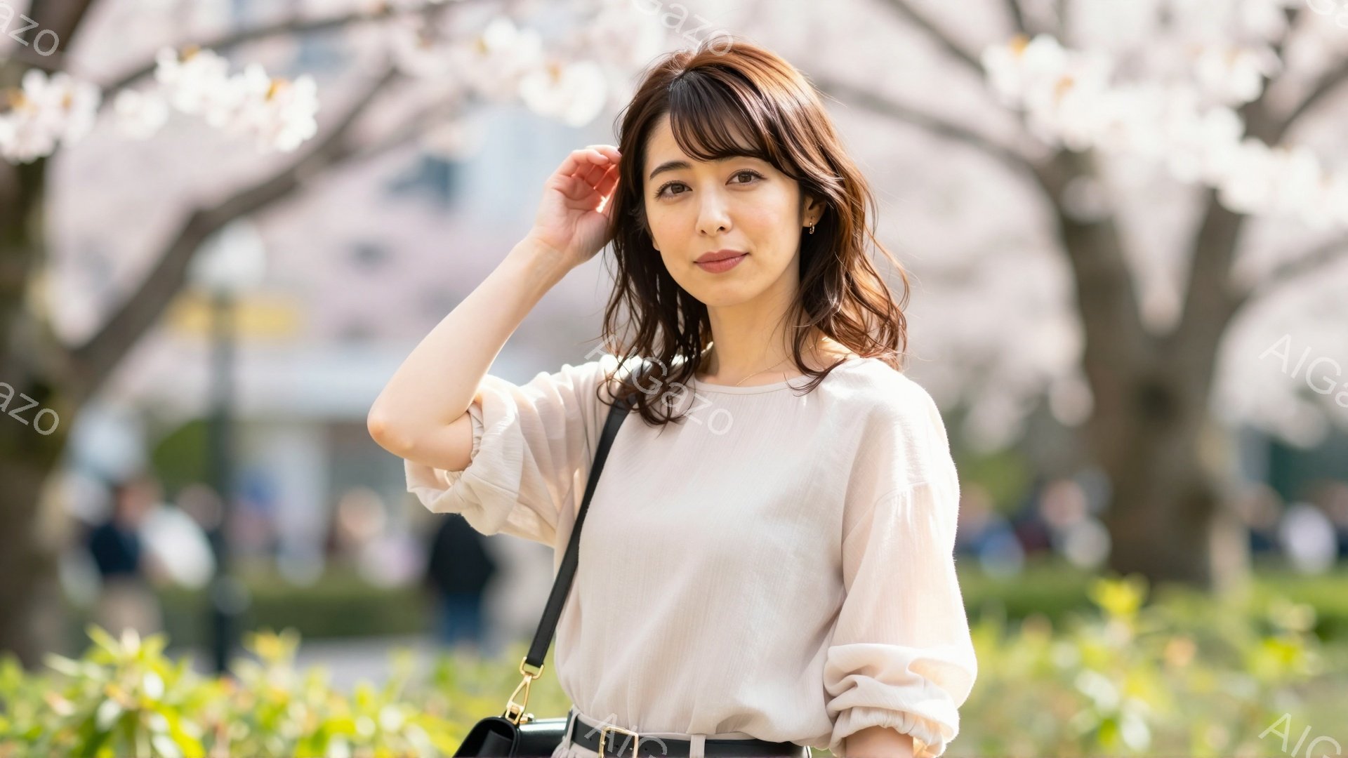 画像には、桜並木の公園でポーズをとる若い女性が写っています。彼女はクリーム色のブラウスに黒いベルトとショルダーバッグを合わせ、髪は肩までの長さで軽くウェーブがかかっています。穏やかな表情で、春らしい柔らかな光の中で、リラックスした雰囲気が漂っています。