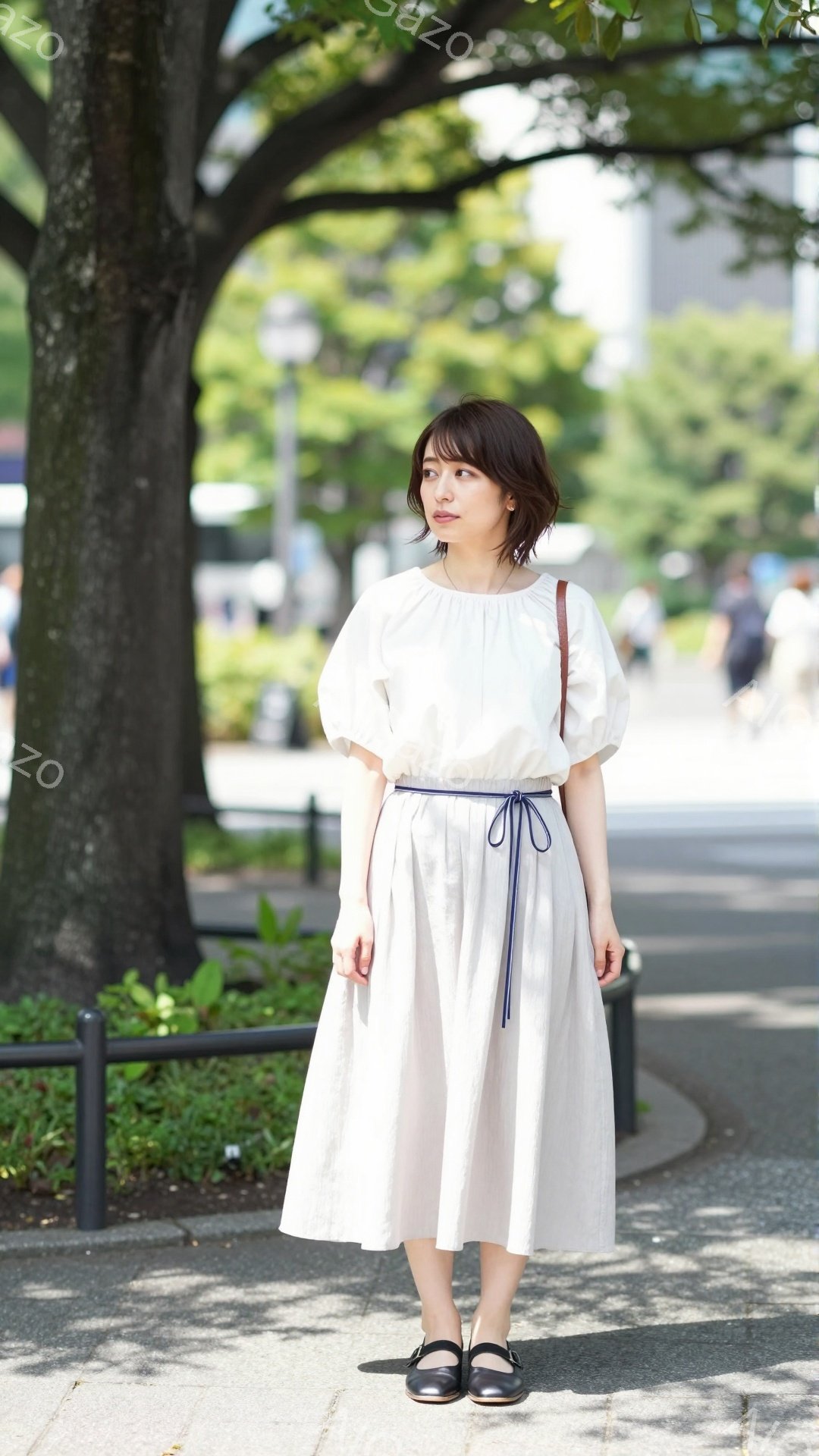 モデルはベージュ色のゆったりとしたワンピースを着ており、ウエストには濃い青色のリボンが結ばれています。彼女は黒髪のボブヘアで、少し微笑んでいるような表情をしています。背景には緑豊かな木々と歩道、そして - AI生成フリー素材