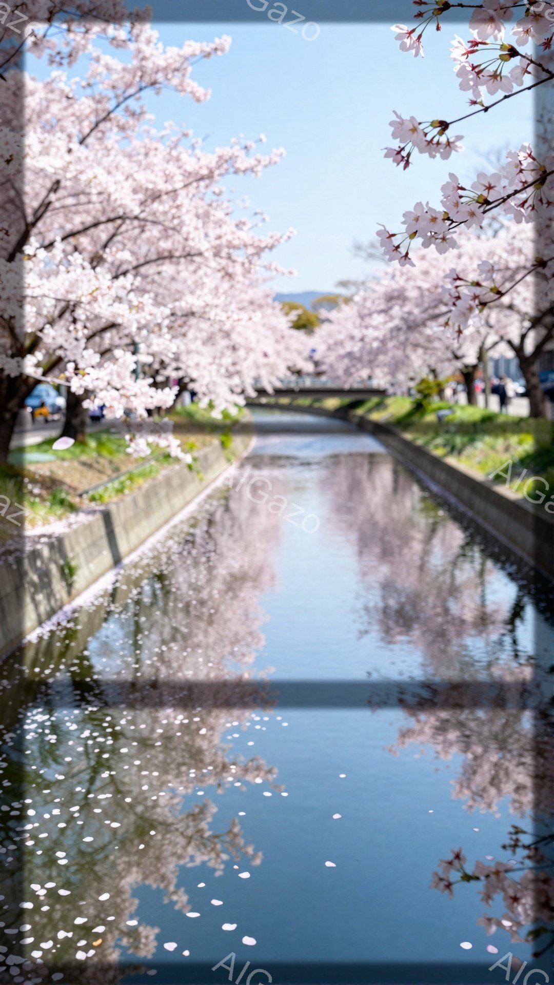 桜並木が続く水路が写真の中心に描かれ、水面には桜の花びらが散りばめられ、穏やかな春の情景が広がっています。空は晴れ、桜並木と水面の反射が美しく、全体的に柔らかな光に包まれた、穏やかで詩的な雰囲気が漂っています。遠くには人影が見え、散歩を楽しむ人々がいるようです。