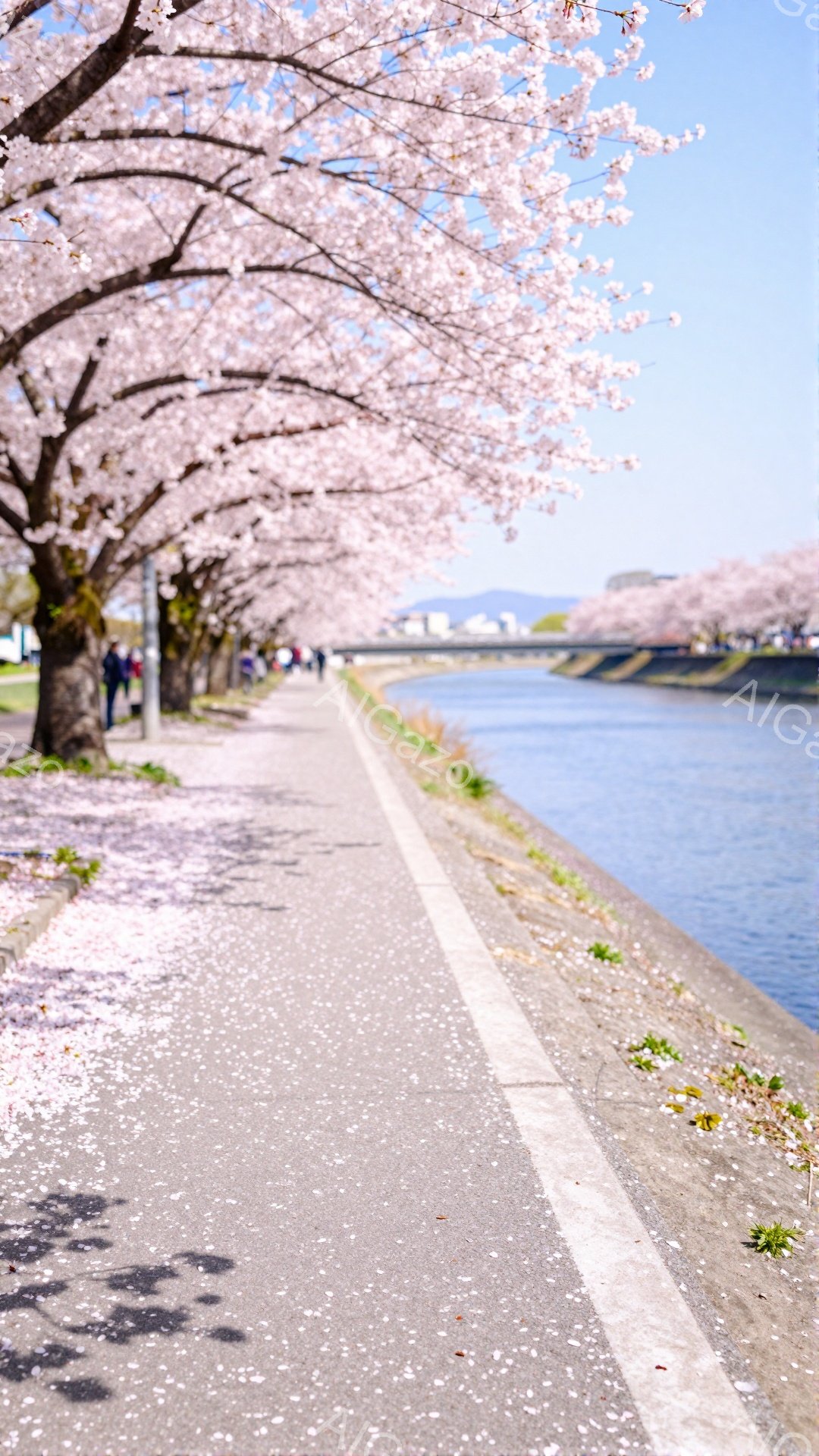 舗装された遊歩道が桜並木に沿って伸びており、地面には散った花びらが敷き詰められています。人々が散歩を楽しんでおり、背景には穏やかな水面と遠くの建物が見えます。全体的に、春の暖かさと穏やかな雰囲気が漂う - AI生成フリー素材