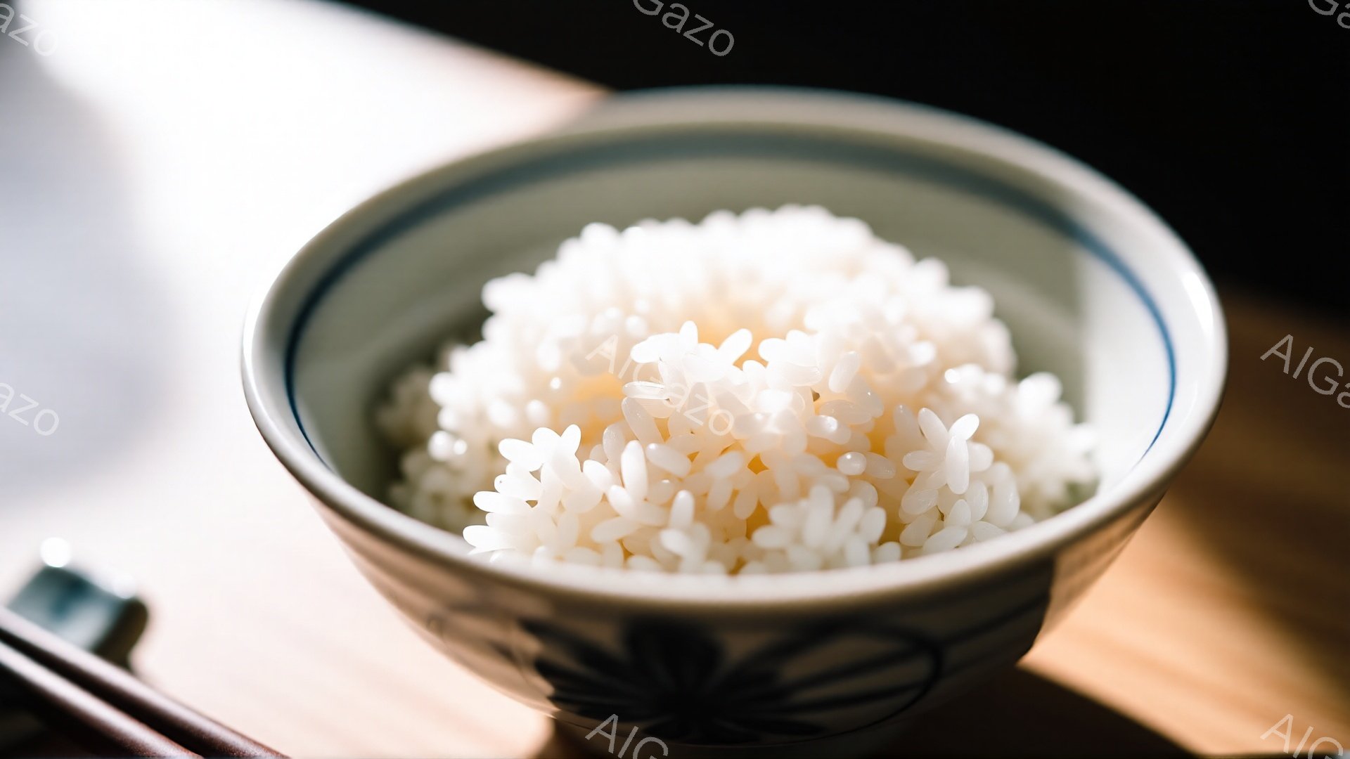 白いご飯が、模様のある茶色の丼に入っています。丼は木製のテーブルの上にあり、奥には箸の一部が見えます。全体的に暖かく、落ち着いた雰囲気で、シンプルながら食欲をそそる構図です。