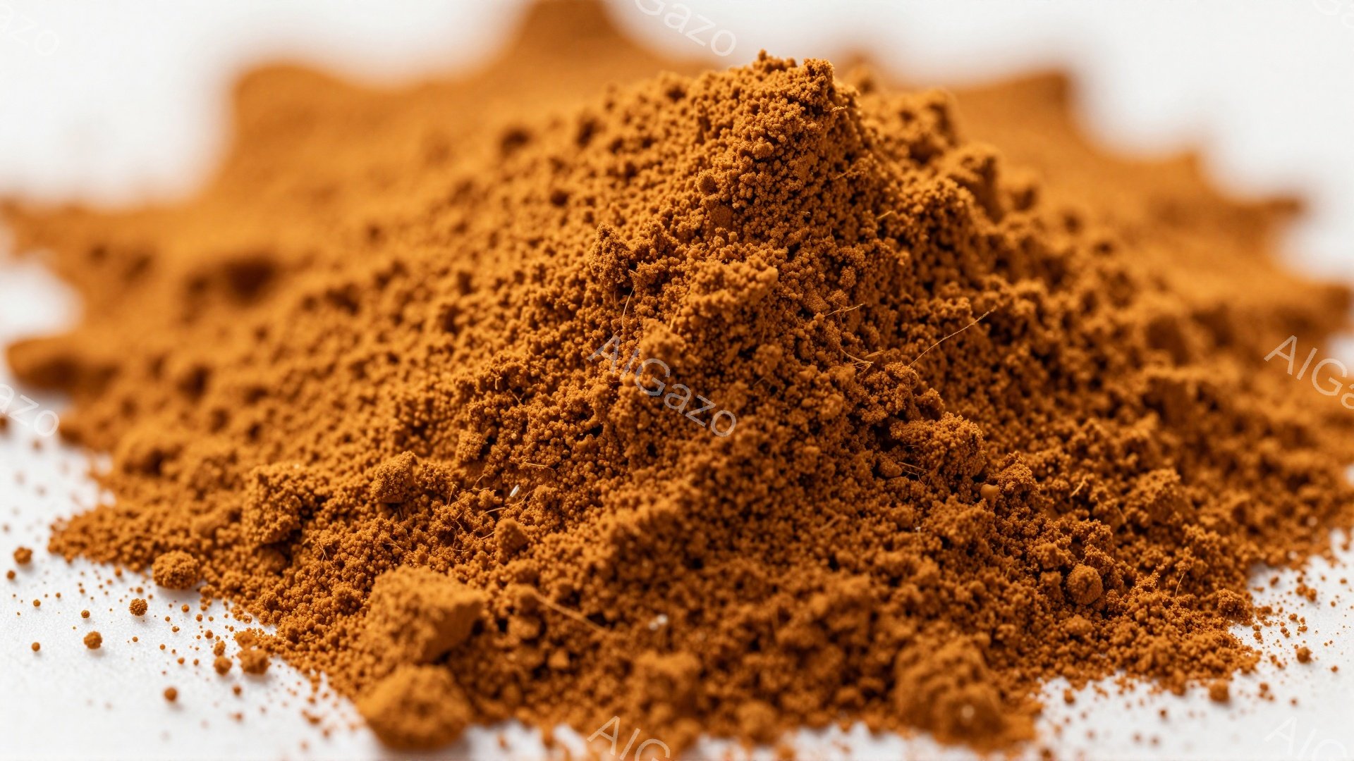 鮮やかな赤褐色の粉末が白い背景に山積みになっている様子が捉えられている。粉末はきめ細かく、まるでスパイスや鉱物のような質感に見える。光が当たって微細な粒子が輝き、全体的に暖かく落ち着いた雰囲気を醸し出している。