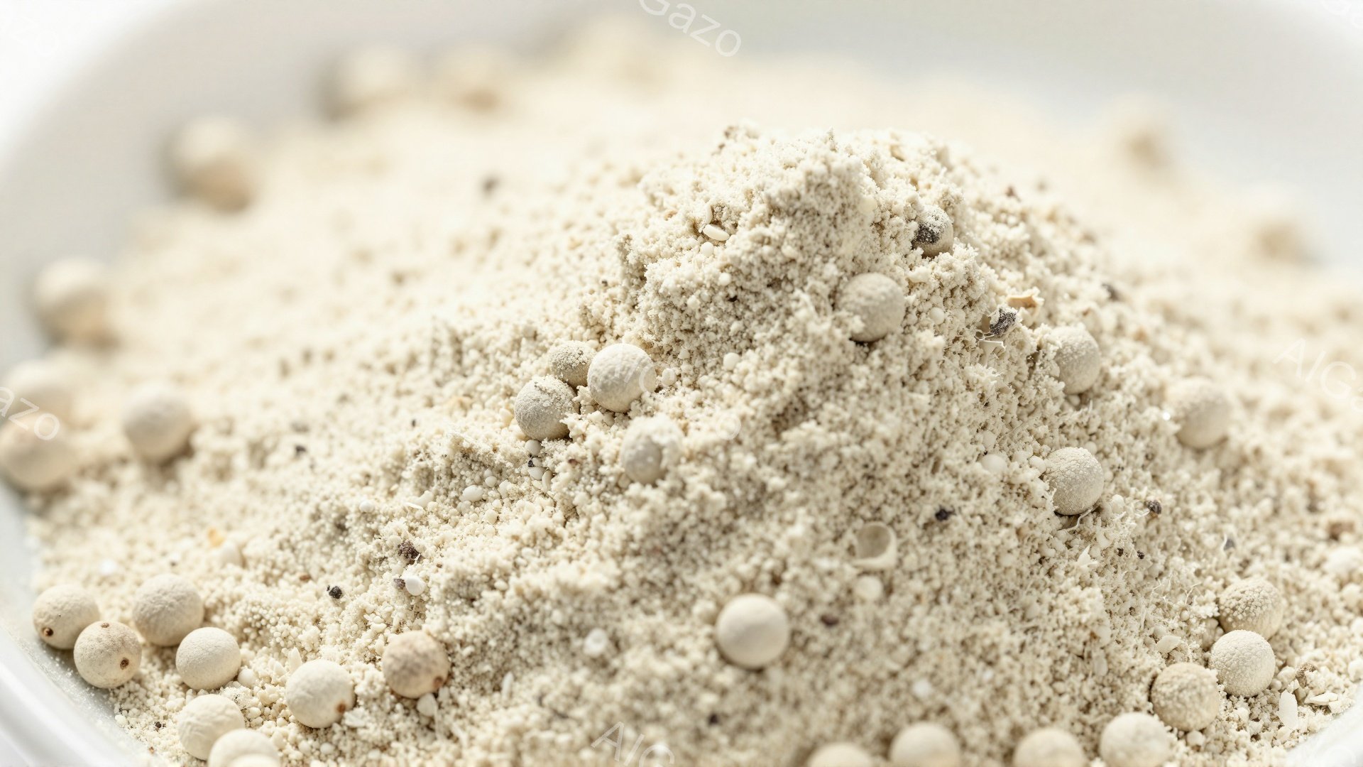 白い器の中に、細かく砕かれた淡いベージュ色の物質と、丸い小さな白い粒が混ざり合って山のように積み重なっています。粒は均一な球体で、砕かれた物質とのコントラストが際立っています。全体的に、調味料や食材の一部であるような印象を与えます。