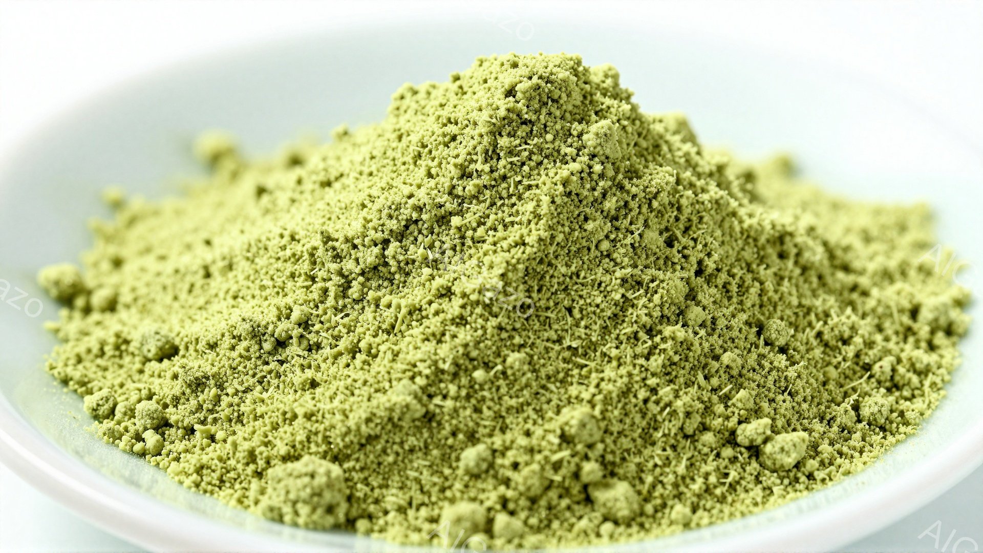 白い器の中に、鮮やかな緑色の粉末が山積みに盛られています。粉末は非常に細かく、抹茶のような、またはハーブパウダーのような印象を与えます。背景は白く、粉末の色を際立たせており、全体的に清潔でシンプルな印象です。