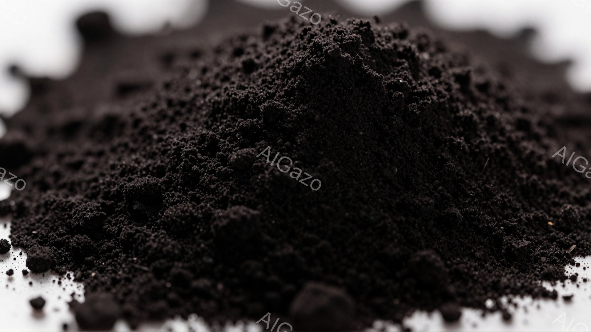 画像は、暗い色の細かい粉末や粒子の山を示しており、質感はざらざらとしています。背景は白っぽく、粉末の暗さと対照的で、その形状は自然に積み重なった様子を彷彿とさせます。全体的に、鉱物や炭のような物質を連想させる、落ち着いた雰囲気です。