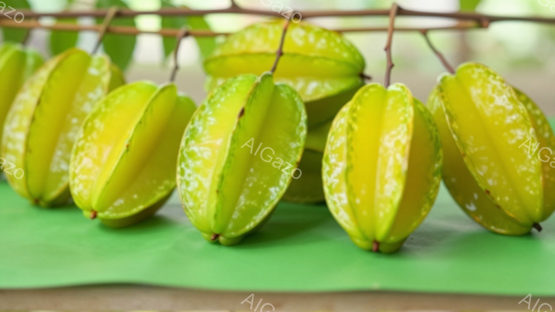 鮮やかな緑色の背景に、星形にカットされた黄色いフルーツが連なっています。フルーツはそれぞれ少しずつ異なった角度でカットされており、表面には小さな水滴が見られます。全体的に明るく、瑞々しい雰囲気が漂っています。