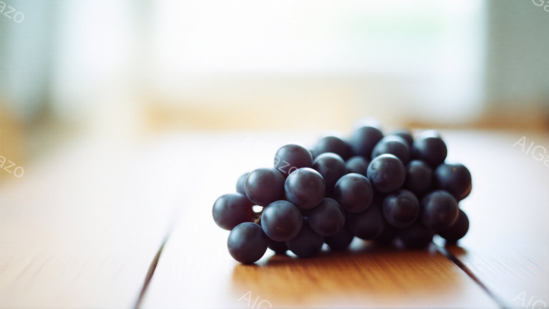 暗い紫色のぶどうの房が、木製のテーブルの上に置かれている。背景はぼやけており、光が差し込んでいる様子から、おそらく屋内であることがわかる。全体的に落ち着いた雰囲気で、ぶどうの質感と色が際立っている。
