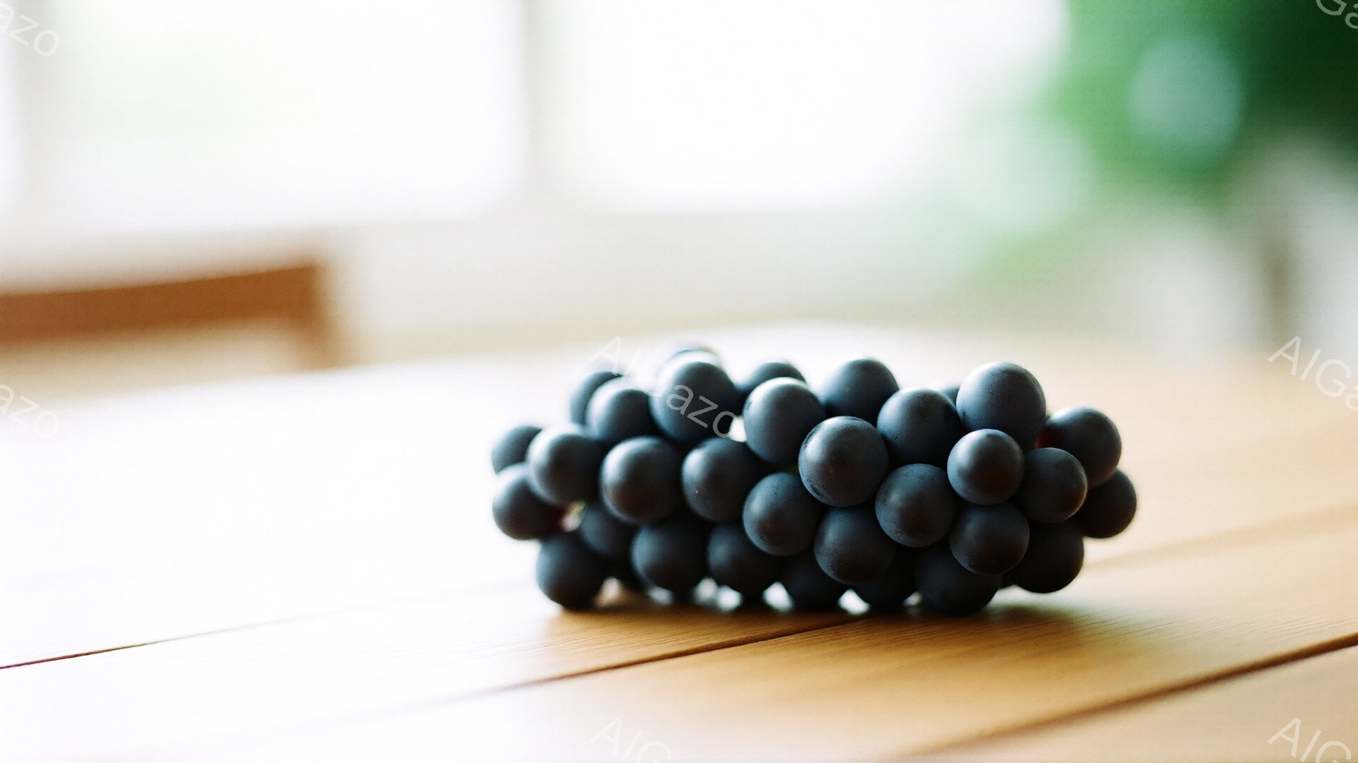 漆黒のぶどうの房が、木製のテーブルの上に置かれている。背景はぼやけた明るい色彩で、室内であることがわかる。全体的に静かで落ち着いた雰囲気で、ぶどうの質感と色が際立っている。