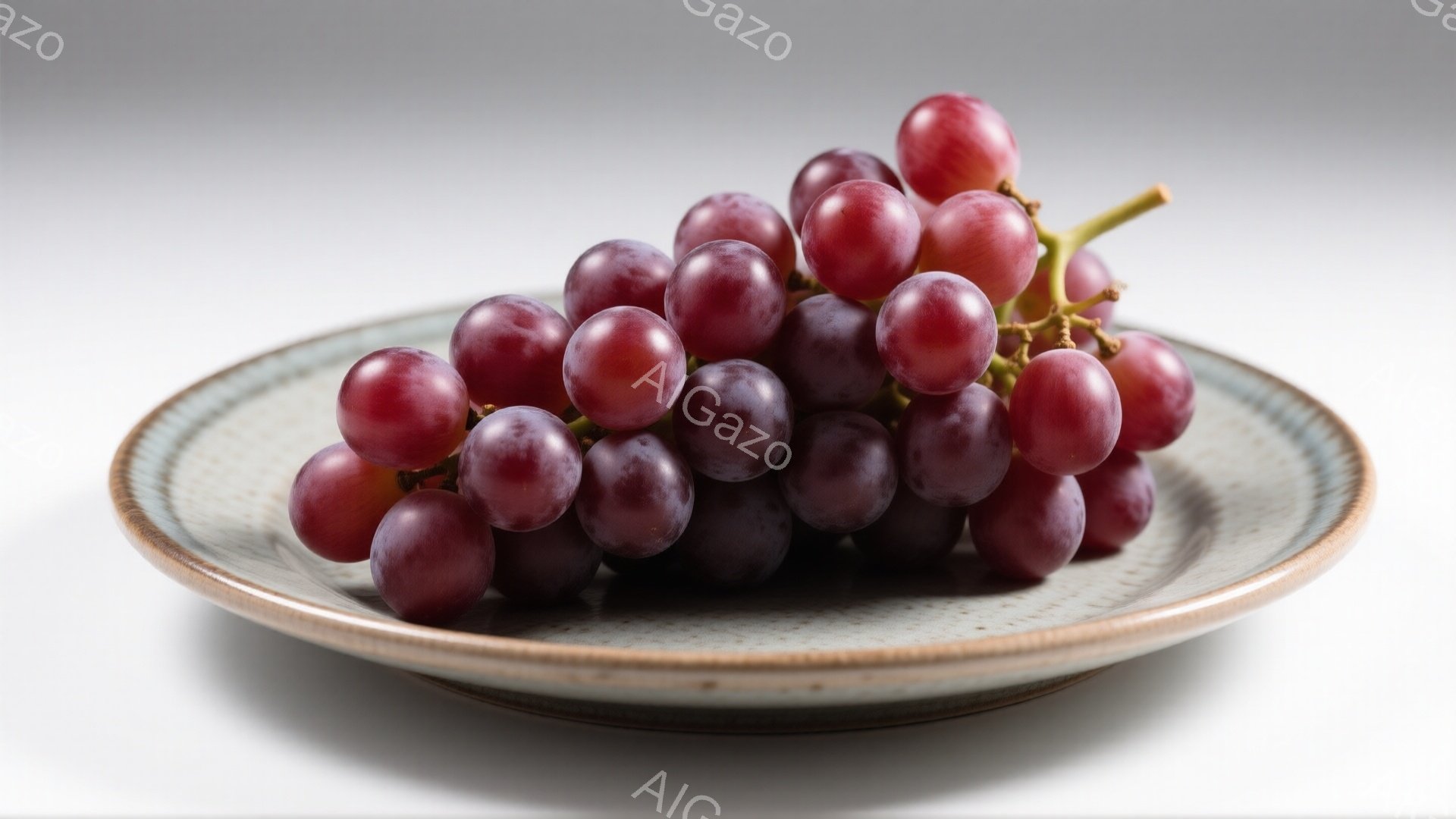 灰色の陶器皿の上に、紫色のぶどうの房が置かれています。ぶどうは丸く、つやがあり、均等に並んでいます。背景は白く、ぶどうの色が際立っています。