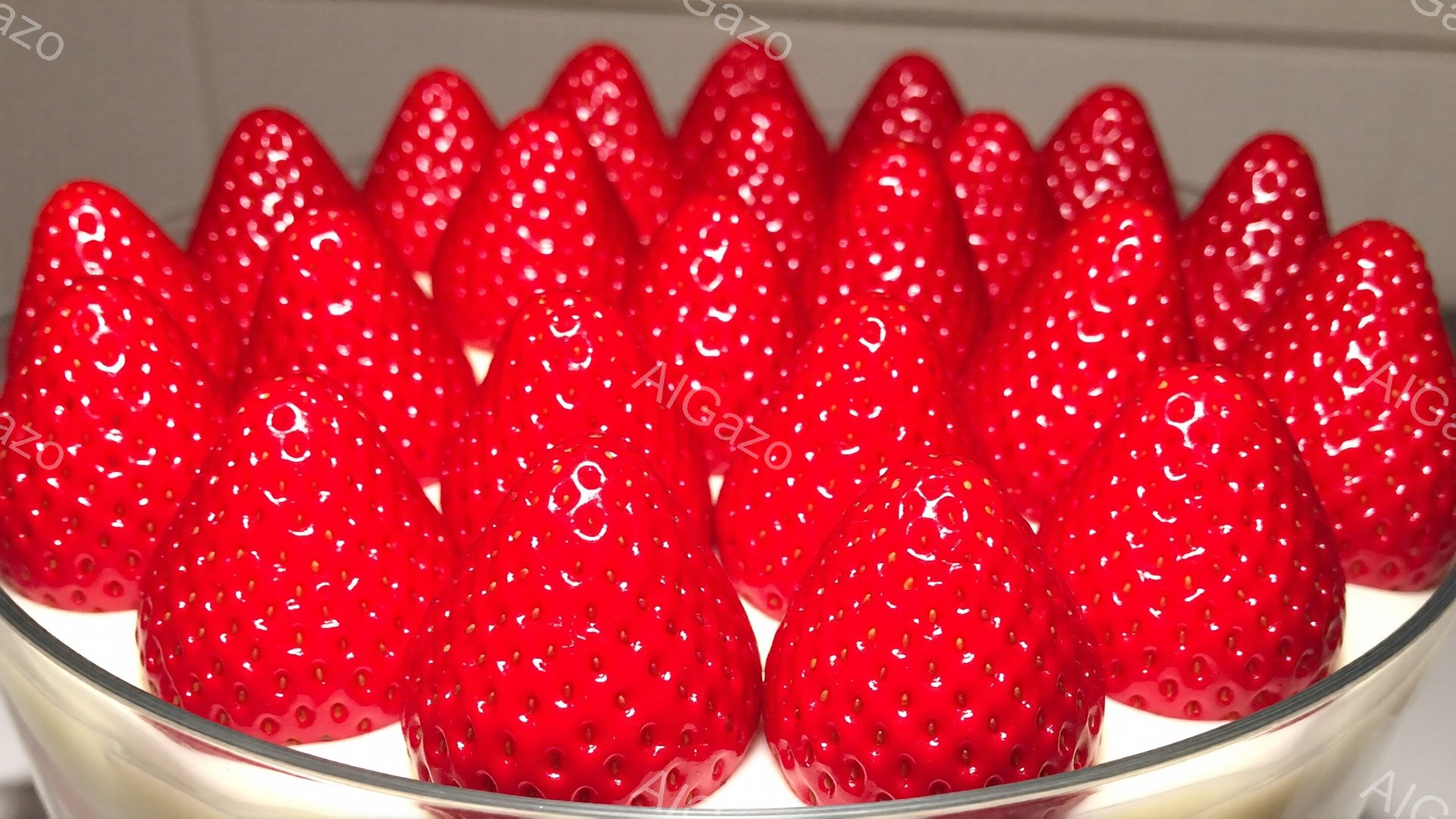 鮮やかな赤いイチゴが、透明な器の中に整然と並んでいます。イチゴはみずみずしく、表面には小さな種が散りばめられており、まるで宝石のように輝いています。背景は白く、イチゴの赤色が際立ち、甘くて美味しそうな雰囲気を醸し出しています。