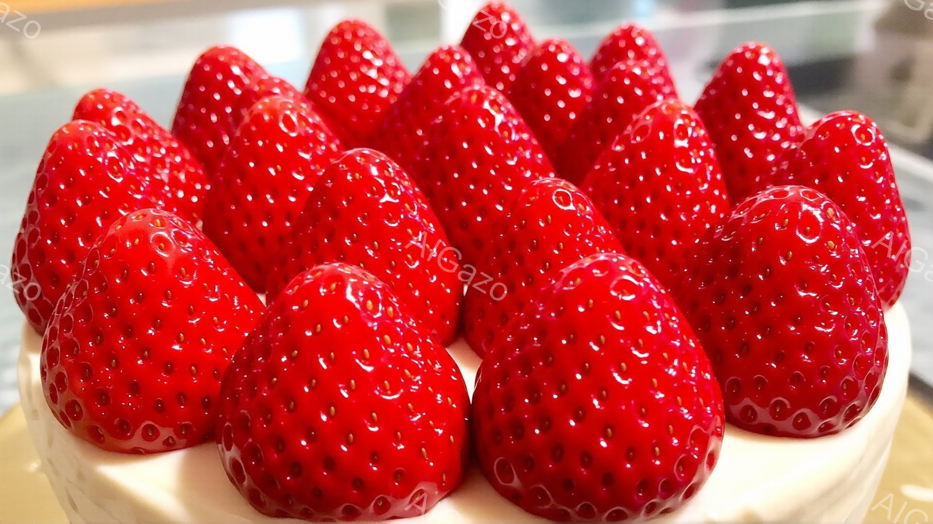 鮮やかな赤色のいちごが、クリーム色のケーキの上にぎっしりと並んでいます。いちごはつややかで瑞々しく、種が細かく点在しているのがわかります。背景はぼかされており、ケーキと苺が際立って見えます。