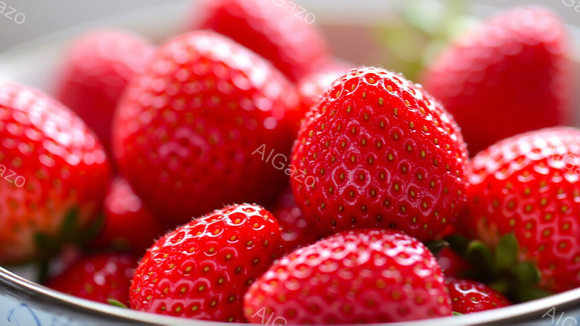 鮮やかな赤いイチゴが密集して写っています。表面には小さな種が散りばめられており、みずみずしく、つやつやと輝いています。背景はぼかされており、イチゴの色がより際立っています。