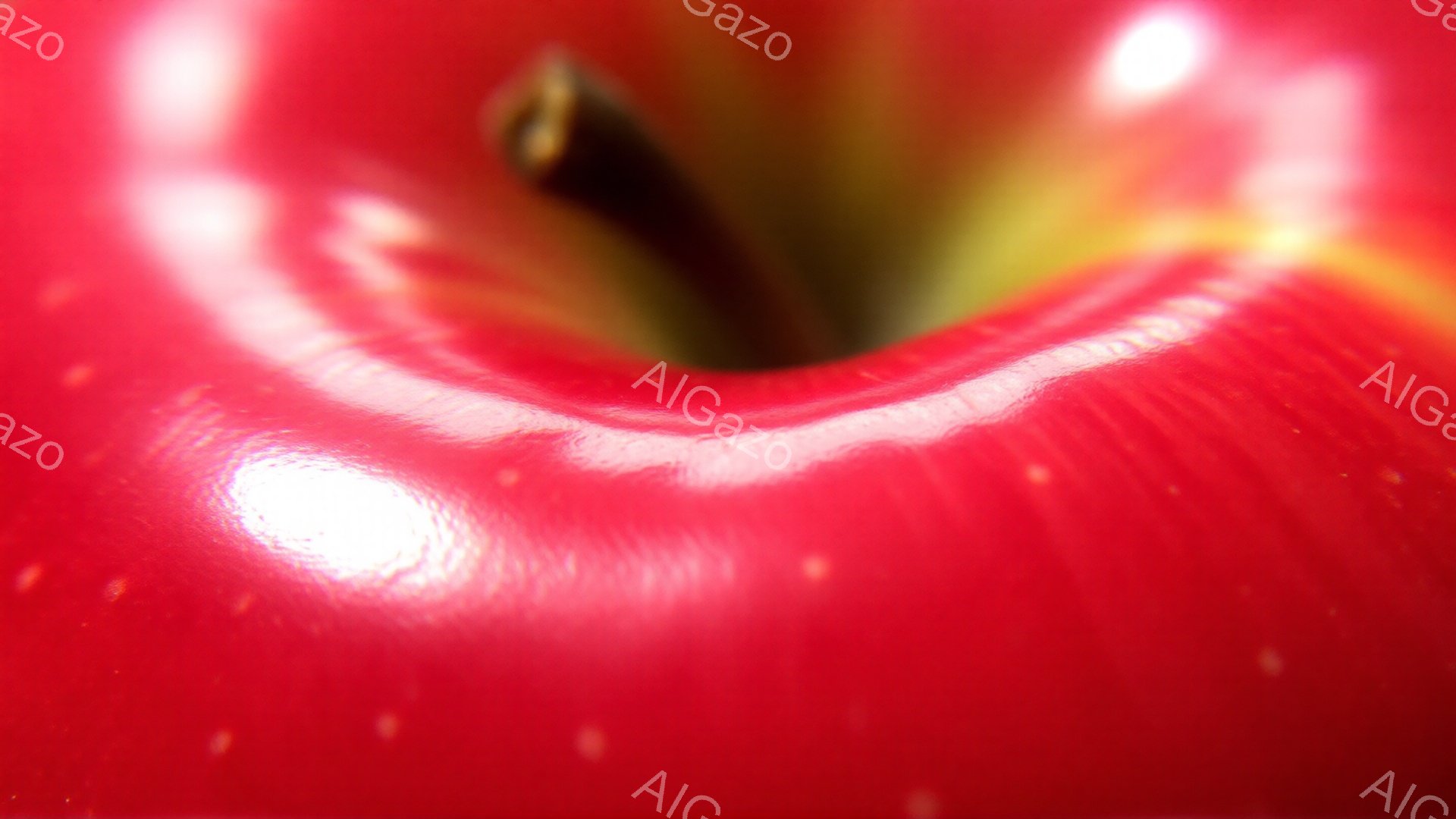 鮮やかな赤いリンゴの接写で、表面の滑らかな曲線と光沢が際立っている。リンゴの中心部には、わずかに茶色い芯が見え、全体的に瑞々しい印象を与える。背景はぼかされており、リンゴの鮮やかさを強調している。