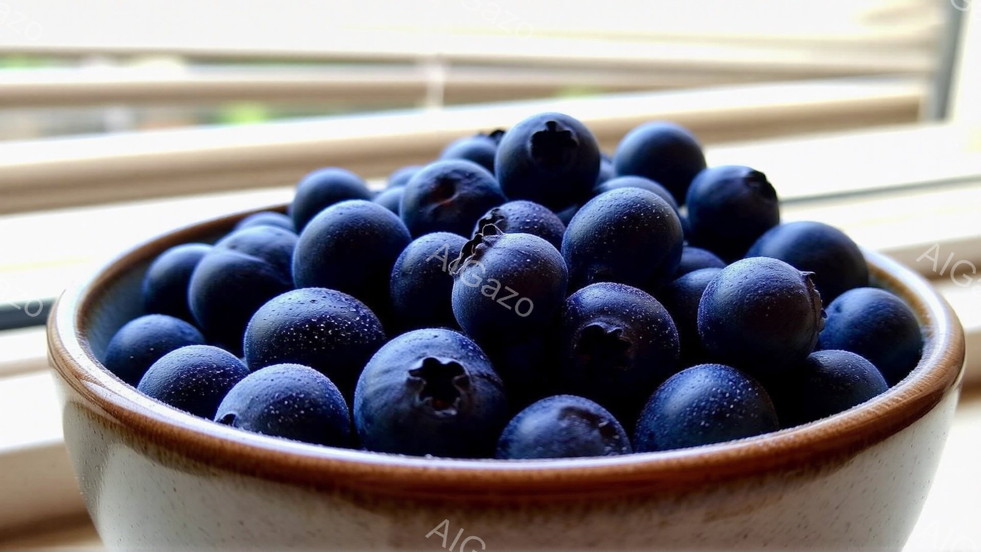 陶器のボウルに新鮮なブルーベリーがたっぷりと入っており、水滴が光ってジューシーさを強調している。背景にはぼやけた窓とカーテンが見え、室内の明るい光がブルーベリーを照らしている。全体的に、新鮮で自然な雰囲気であり、食欲をそそる構図となっている。