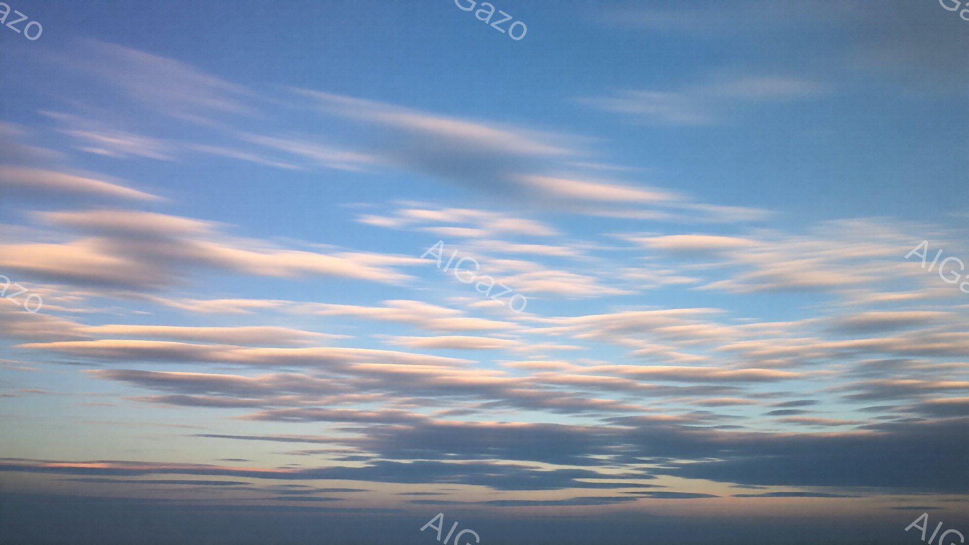 広大な空に、淡いピンクと白の雲がもくもくと広がっている。雲は羊の毛のようにふっくらとしており、太陽の光を浴びて黄金色に染まっている。全体的に穏やかで夢幻的な雰囲気が漂い、まるで絵画のような美しい空である。