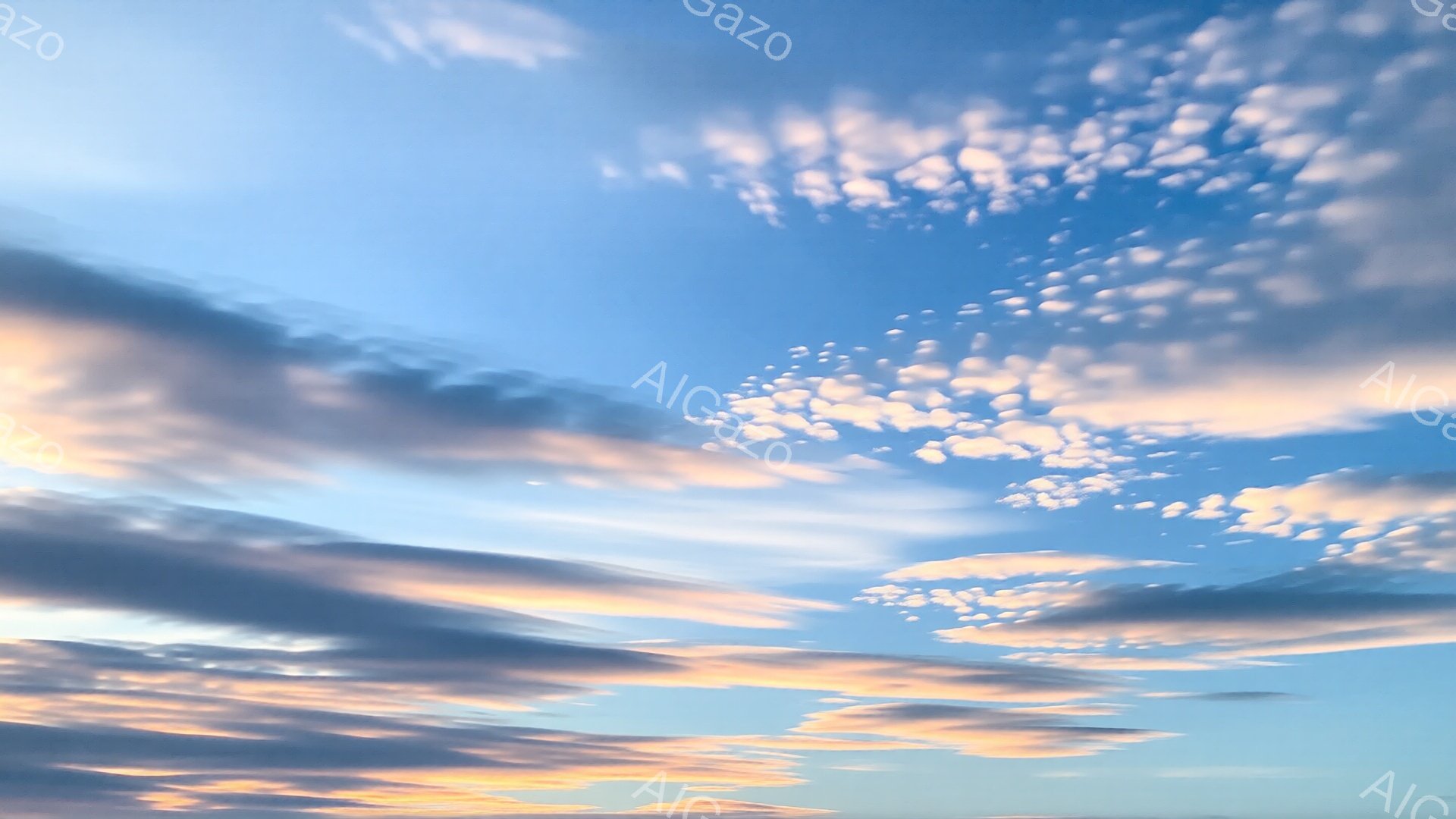 鮮やかな青空に、オレンジ色や薄いピンク色の雲が広がっている。雲は様々な形をしており、まるで絵の具を混ぜたような美しいグラデーションを描いている。穏やかで暖かく、夕焼けのような、または日の出前の空のよう - AI生成フリー素材