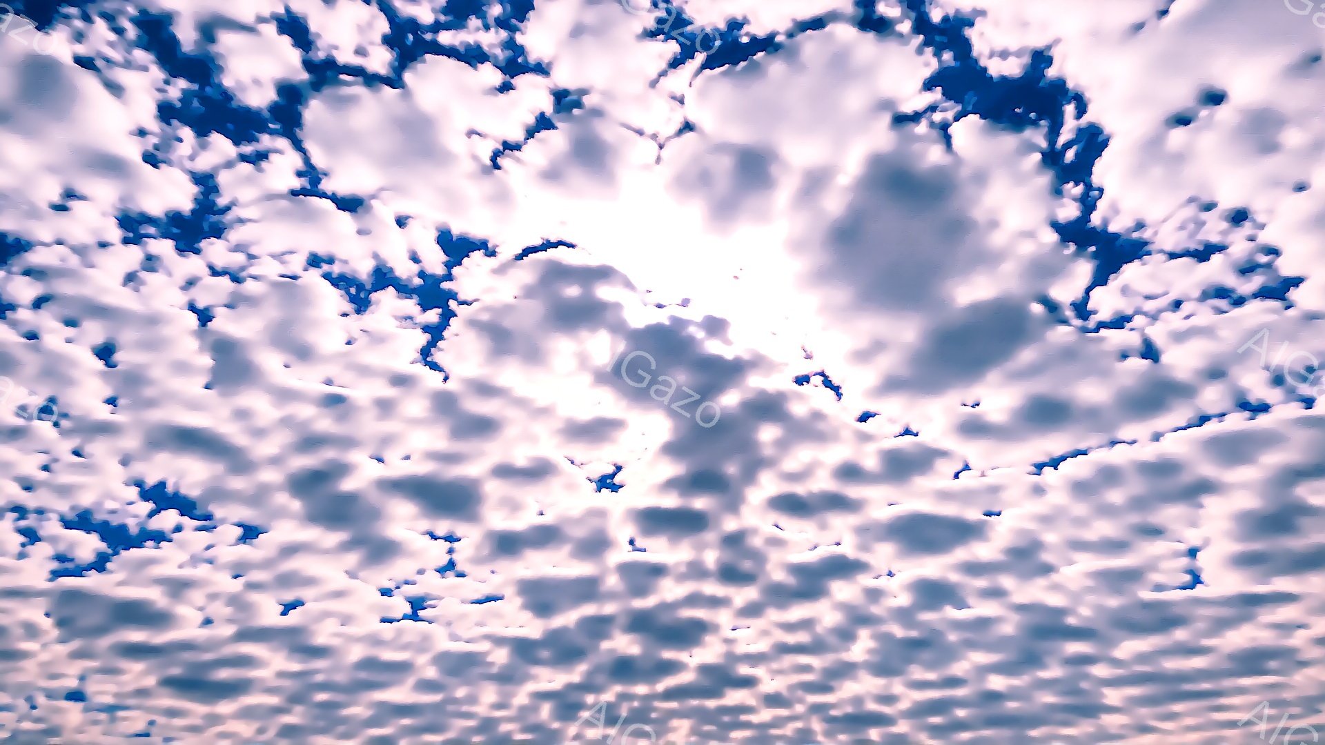 空一面に細かいうろこ雲が広がり、まるで波のような模様を描いています。太陽が雲の隙間から強く差し込み、画面中央で光り輝いており、雲の影がコントラストを生み出しています。晴れ渡った青空と白い雲の組み合わせ - AI生成フリー素材