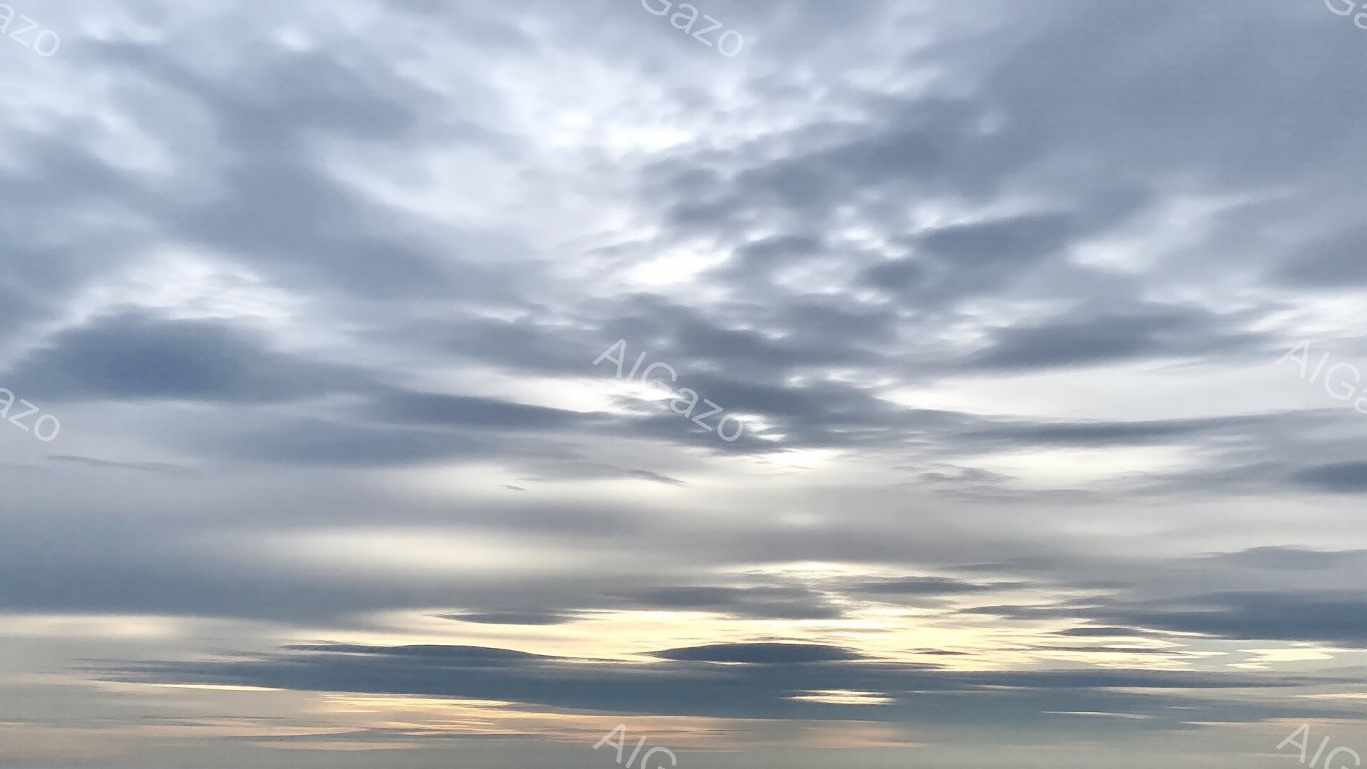 空一面に厚い雲が広がり、夕焼けの名残が雲の隙間から金色に漏れ出している。雲の形はまるで波のようにうねり、重厚感と神秘的な雰囲気を醸し出している。地平線付近はわずかに明るいオレンジ色で、穏やかさと静寂を感じさせる。