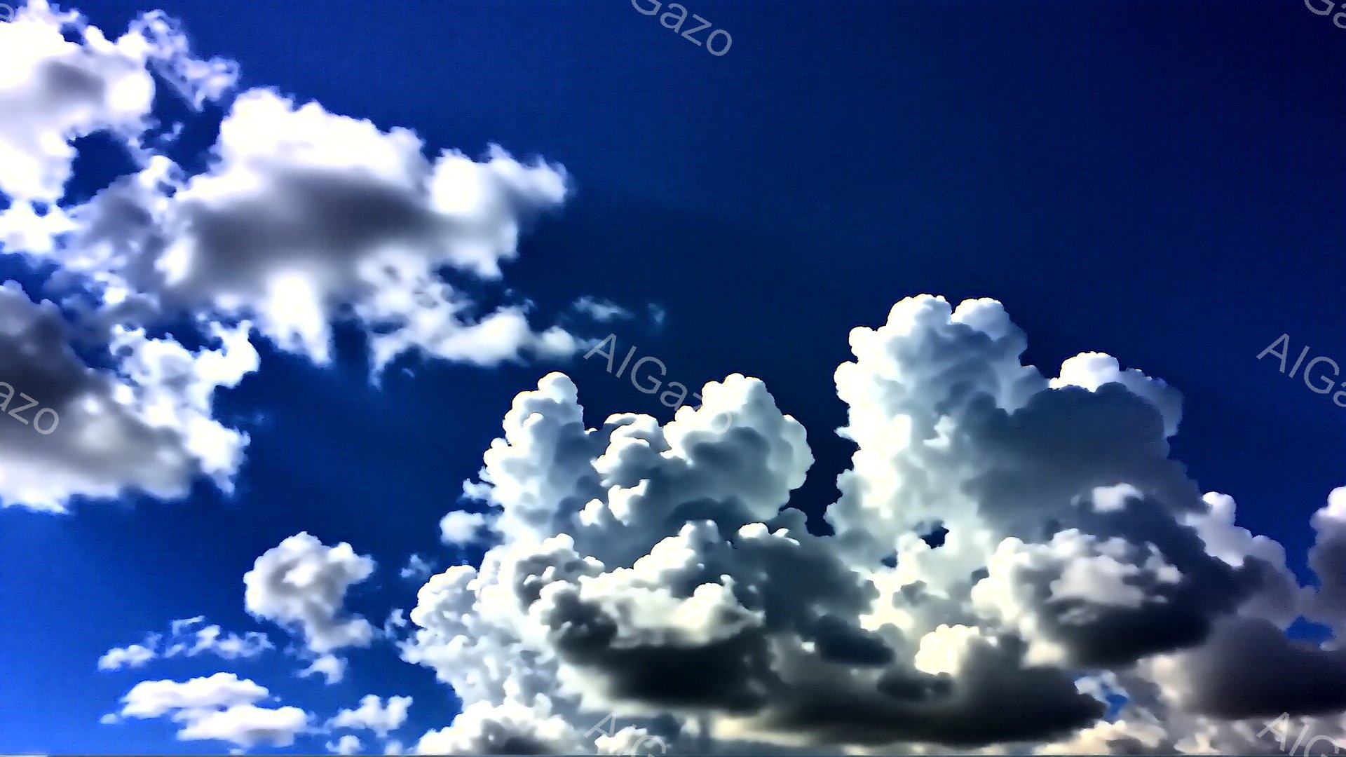 鮮やかな青空に、白いもくもくとした雲が広がっています。雲は大きく、綿のようにふかふかとしており、太陽の光を浴びて白く輝いています。全体的に明るく爽やかな、夏の日の空の雰囲気です。