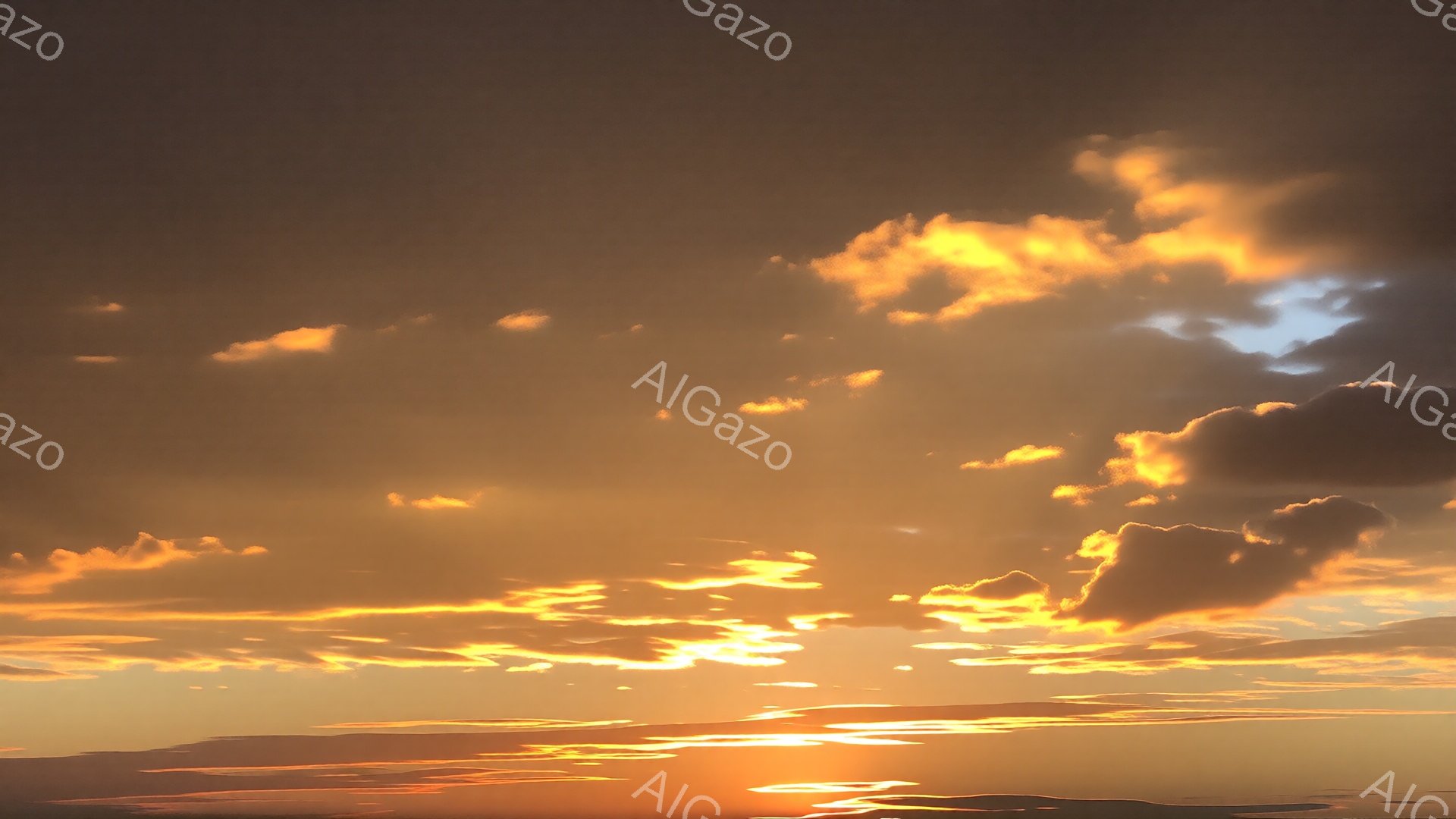 燃えるような夕焼け空が広がり、オレンジと金色の雲が空全体を覆っている。地平線付近は特に明るく、水面には太陽の光が反射してキラキラと輝いている。雲の形は多様で、力強く、穏やかな印象を与える空景である。
