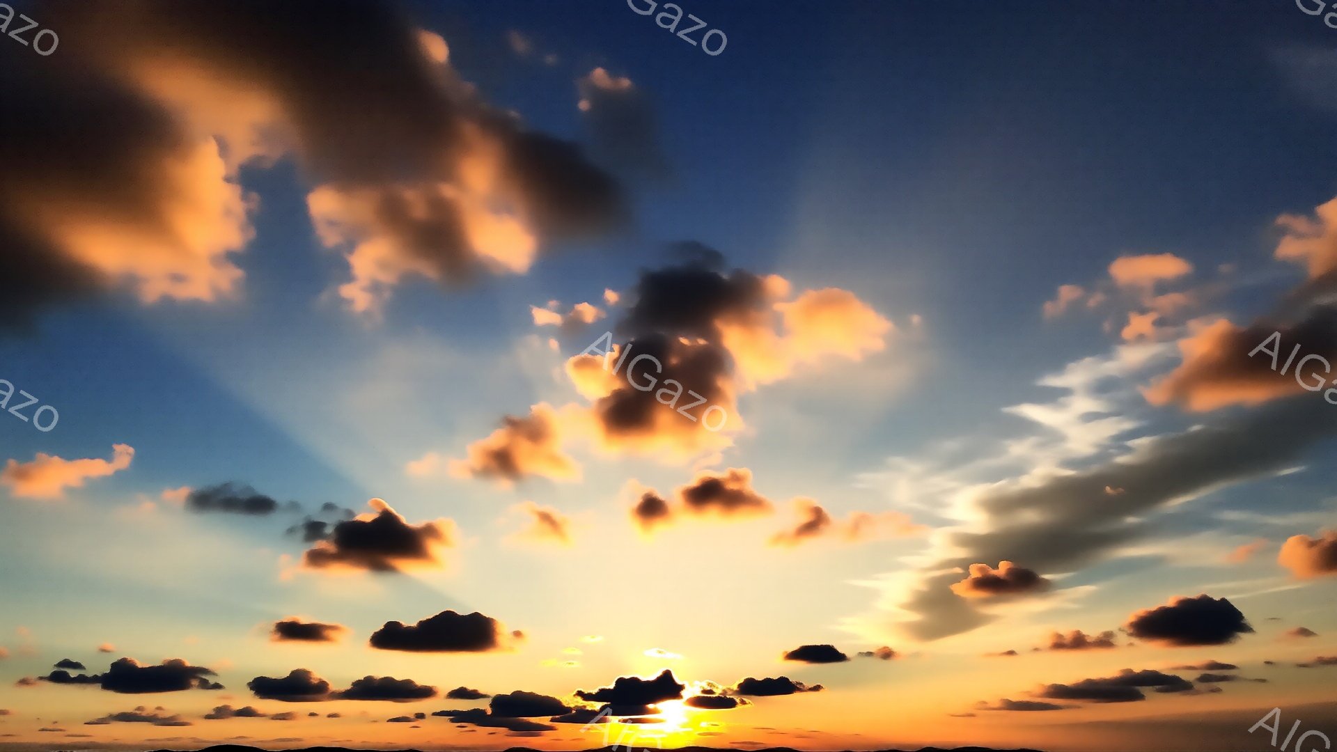 燃え盛る夕焼け空が印象的な写真です。オレンジと黒の雲が空一面に広がり、太陽の光線が雲間から力強く差し込んでいる様子が捉えられています。地平線にはぼんやりと山並みが確認でき、穏やかで壮大な雰囲気が漂っています。