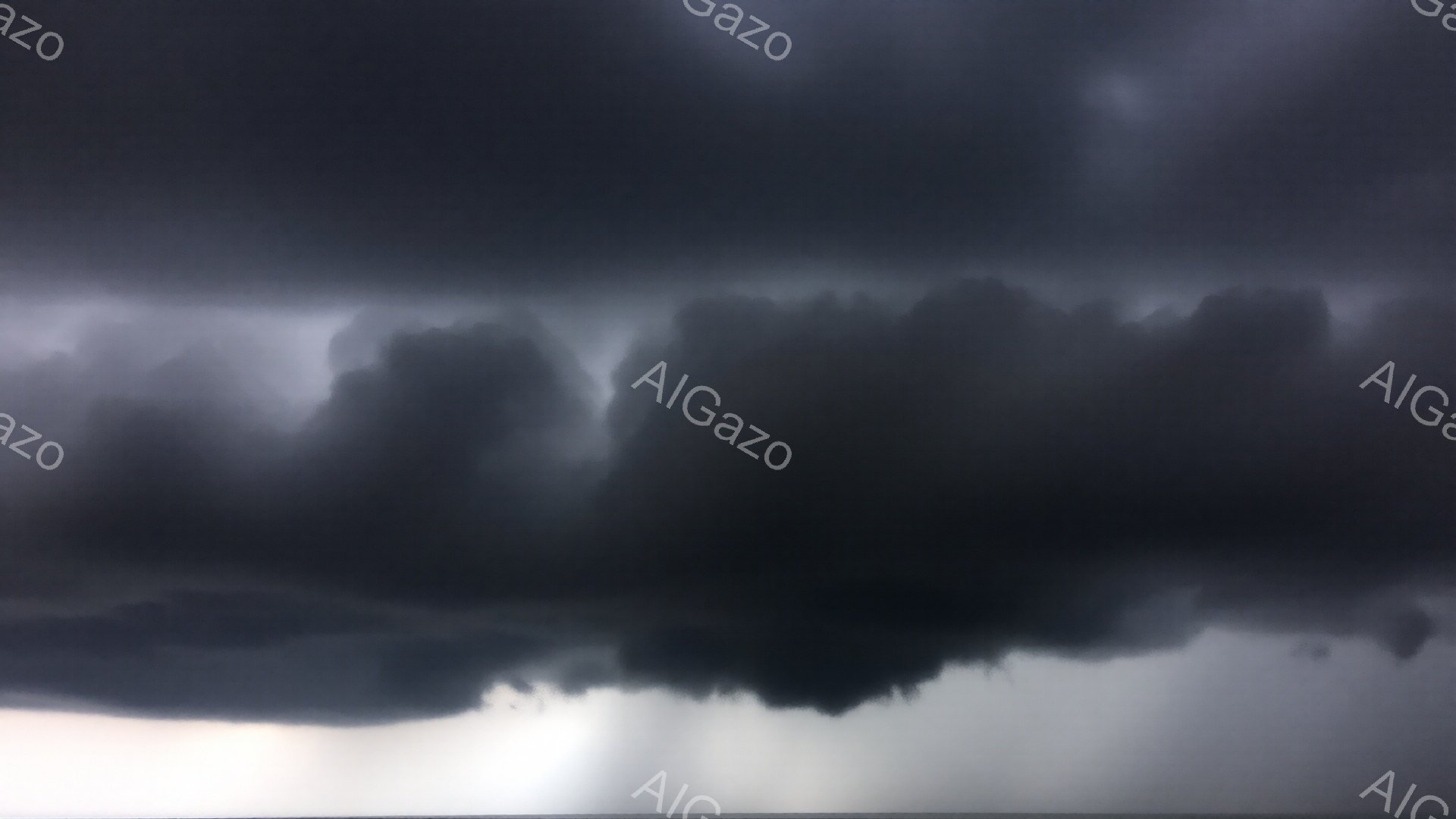 濃い雨雲が空一面を覆い、地平線には薄明かりが残っている。雲は重く、まるで世界を飲み込もうとしているような、圧倒的な迫力がある。雨が雲から滴り落ちており、陰鬱で嵐の前の静けさのような雰囲気が漂っている。 - AI生成フリー素材