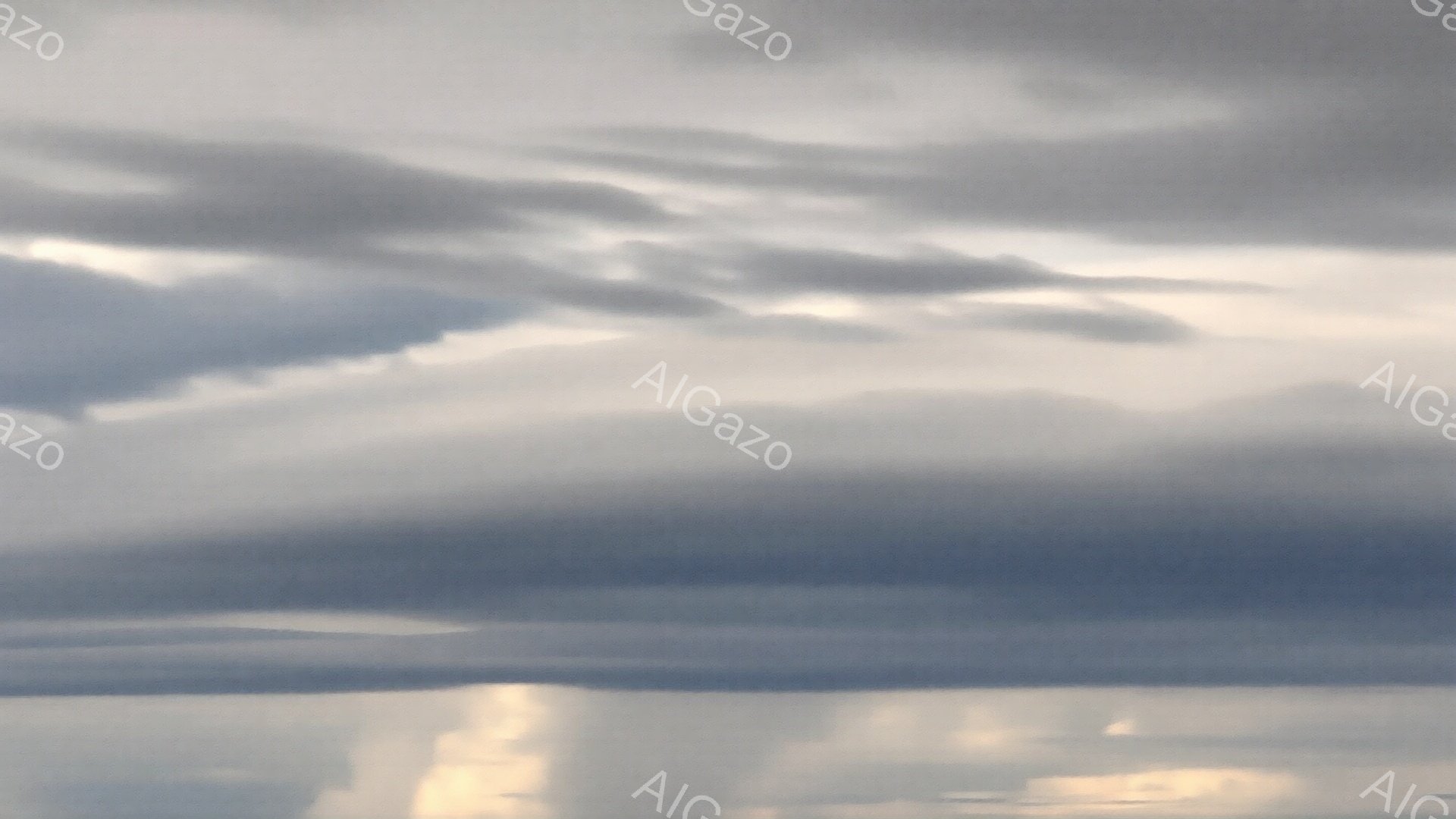 灰色の雲が空一面に広がり、重厚な雰囲気を醸し出しています。雲の隙間から差し込む光が、わずかに地表を照らしており、光芒が確認できます。全体的に、雨が降り出す直前の、静かで少し憂鬱な天候を表しています。