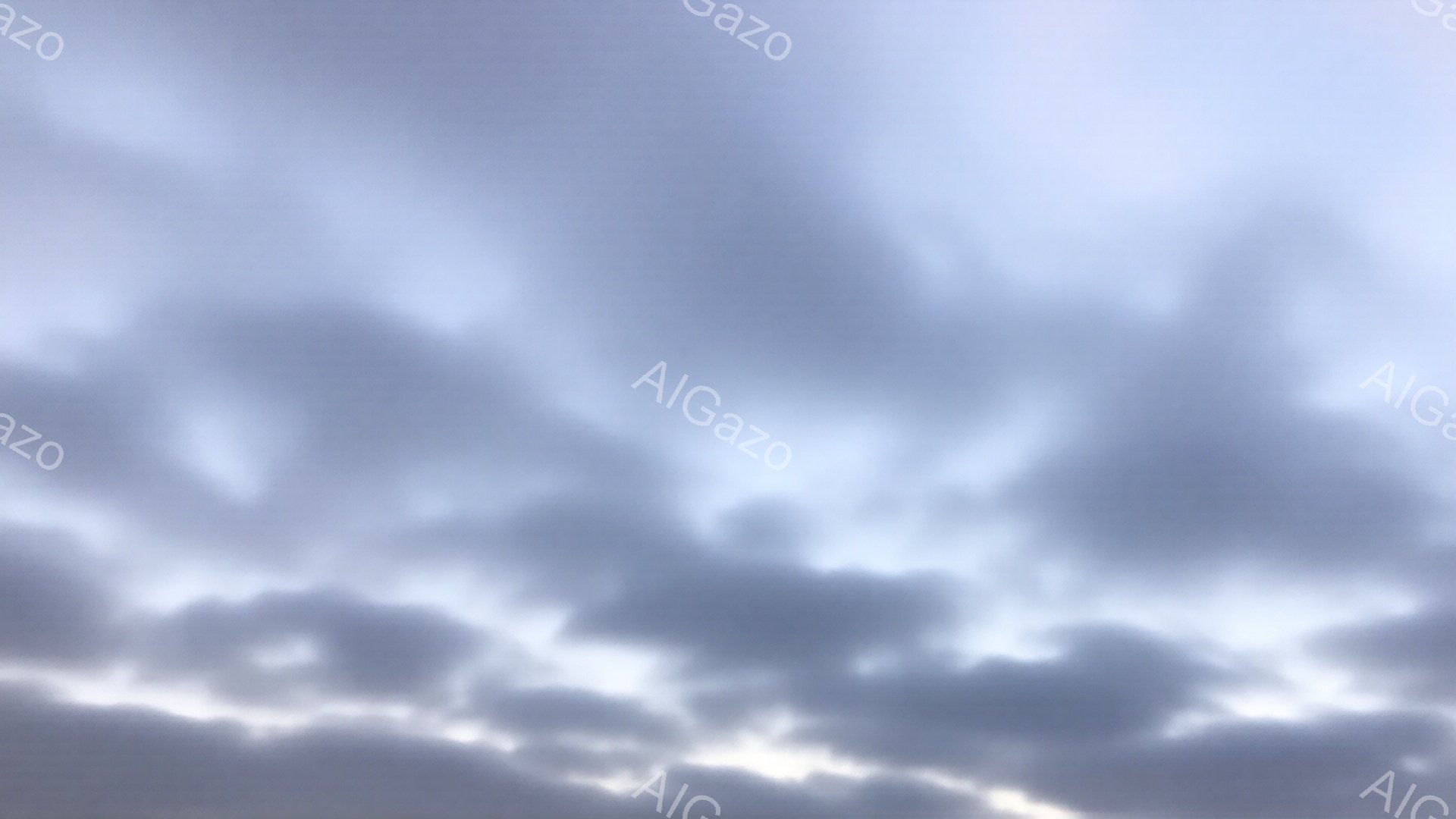 空は厚い雲に覆われ、明るい光が雲の間から差し込んでいる。雲は灰色と白の様々な色合いで、重厚感と静けさを感じさせる。全体的に、雨が降りそうか、または雨上がりの空の様子がうかがえる。