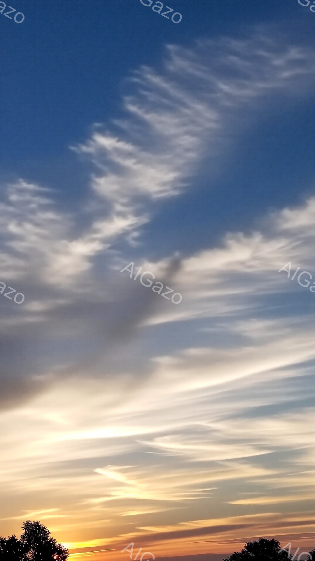 空は夕焼けの名残でオレンジ色から薄い青へとグラデーションを描き、繊細な雲が広がり、まるで筆で描いたような美しい模様を作り出している。地平線付近には緑色の木々がシルエットとして見え、静かで穏やかな雰囲気 - AI生成フリー素材