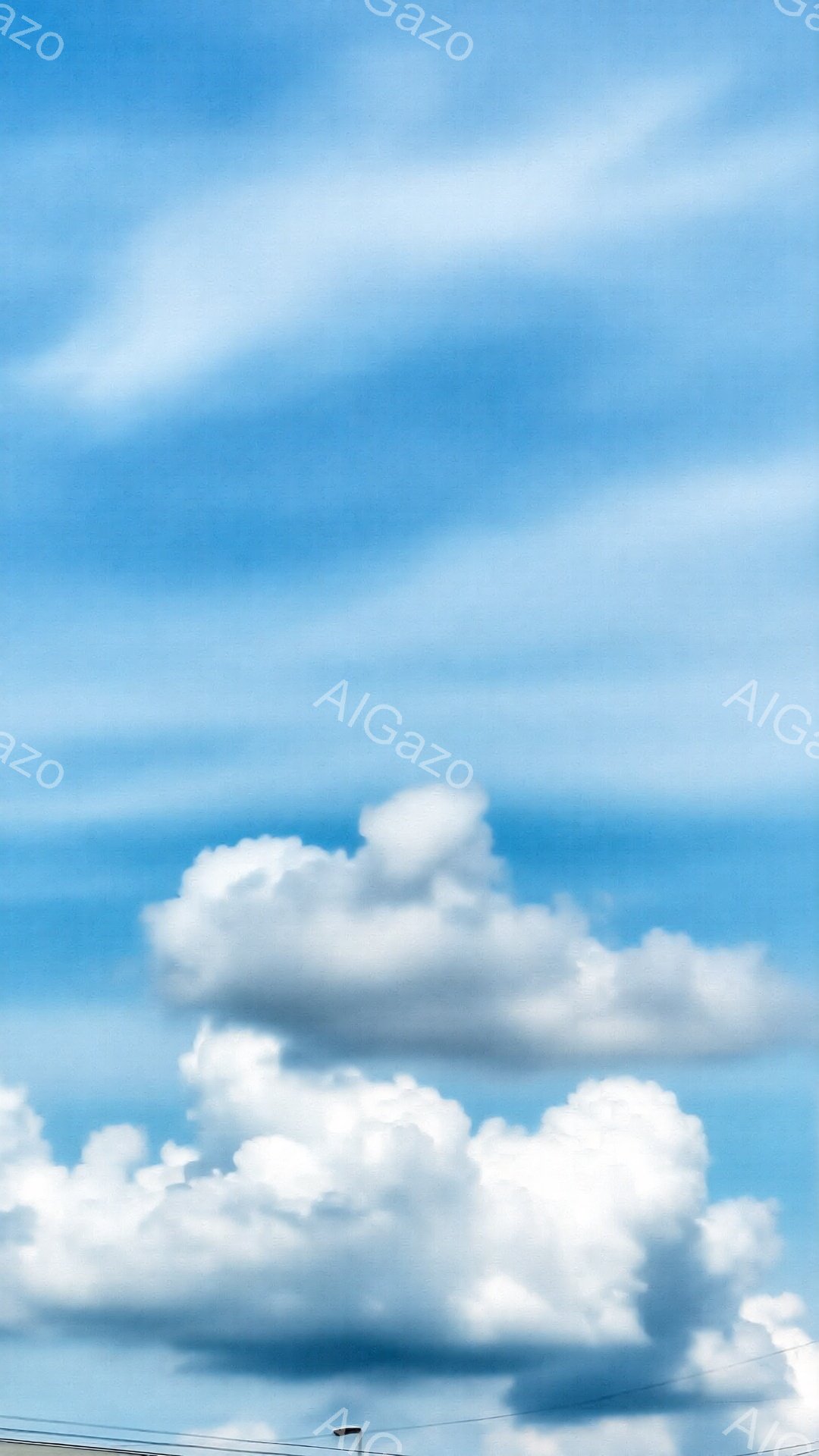 鮮やかな青空に、白いふわふわとした雲が浮かんでいます。雲は様々な形をしており、まるで綿菓子のように見えます。画面下部には建物の屋根の一部と街灯が見え、晴れた日の穏やかな空模様を表しています。