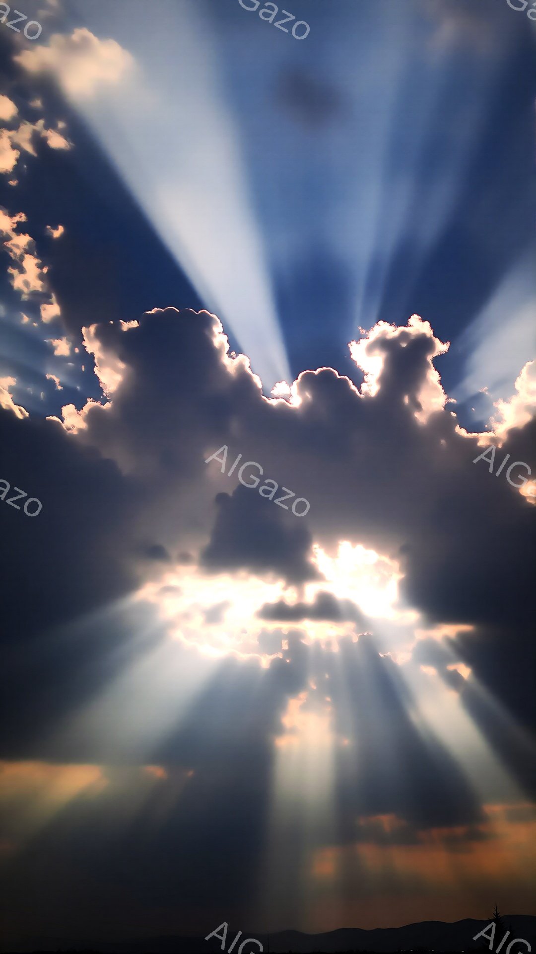 劇的な空の風景で、厚い暗雲が光の筋を強烈に引き出している。太陽光線は雲間から差し込み、空全体に神々しい黄金色の輝きを添えている。地平線にはぼんやりとした山の輪郭が見え、風景に奥行きを与えている。